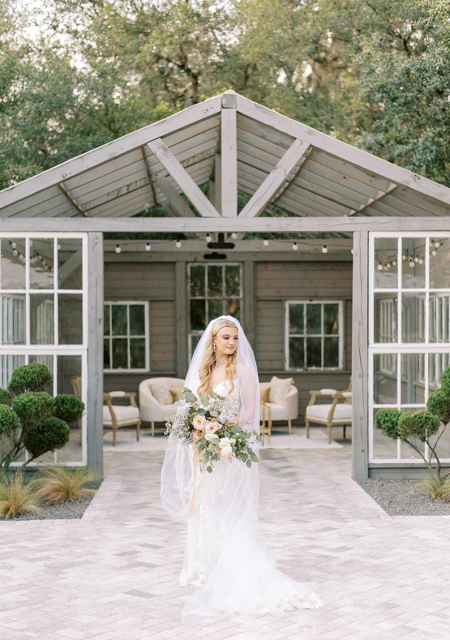 bride poses in front of greenhouse at Mill Pond Estate with veil around shoulders 
