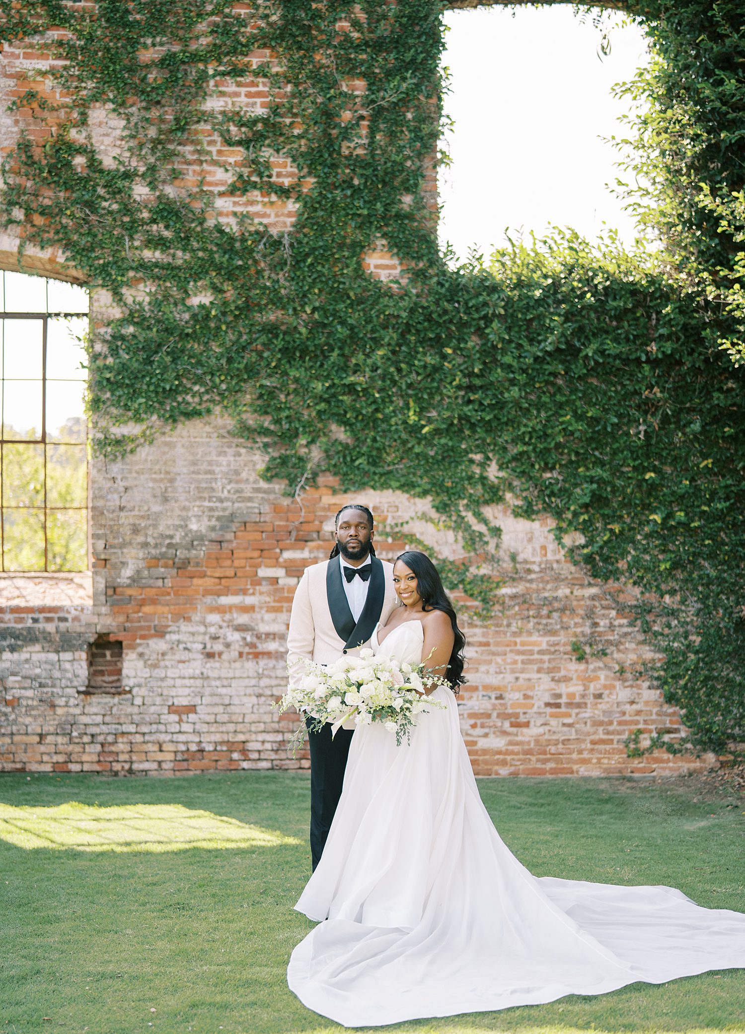 bride and groom hug in front of brick wall covered in ivy at The Bibb Mill Event Center