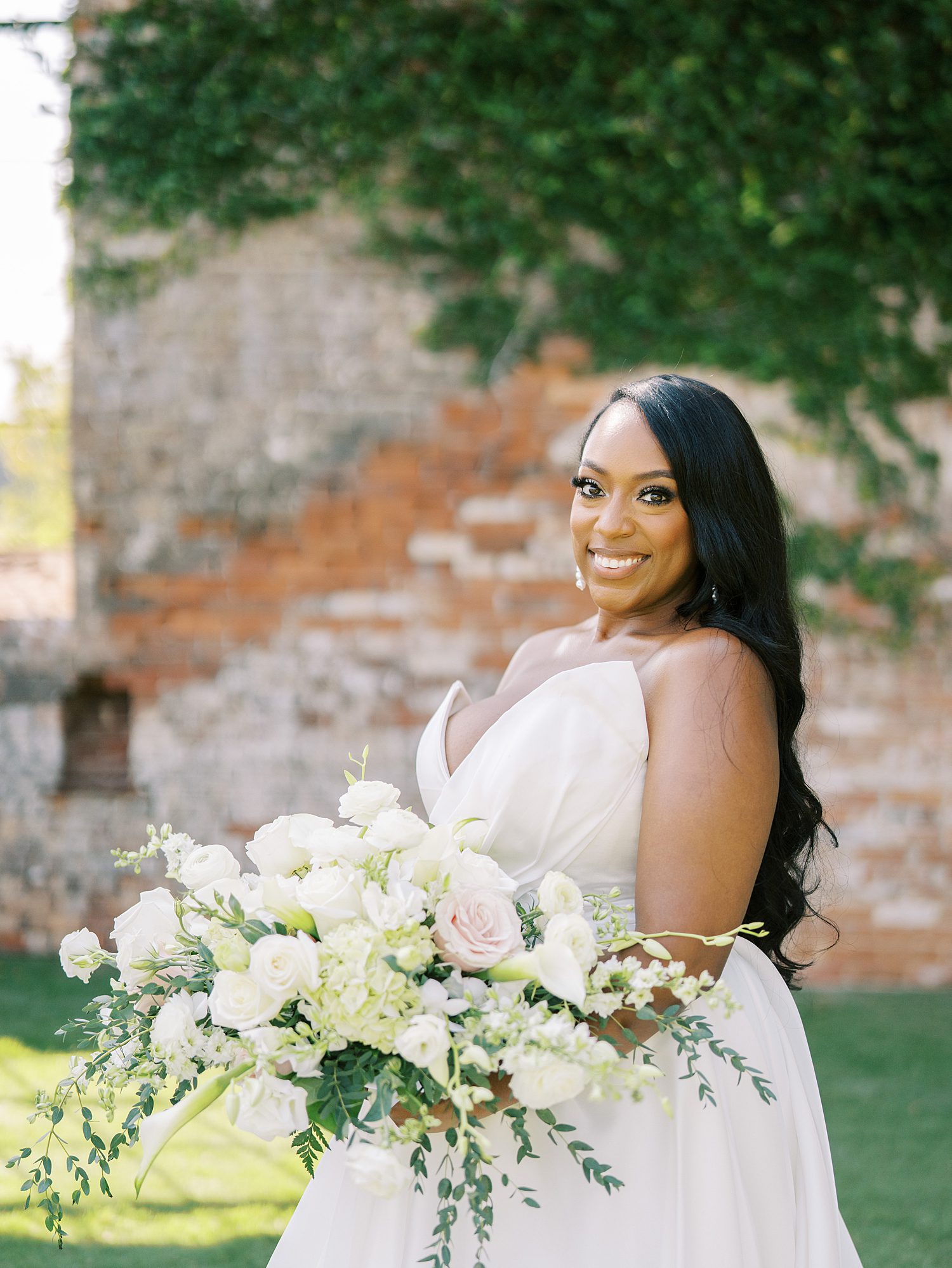 bride holds bouquet of ivory flowers in front of brick wall at The Bibb Mill Event Center