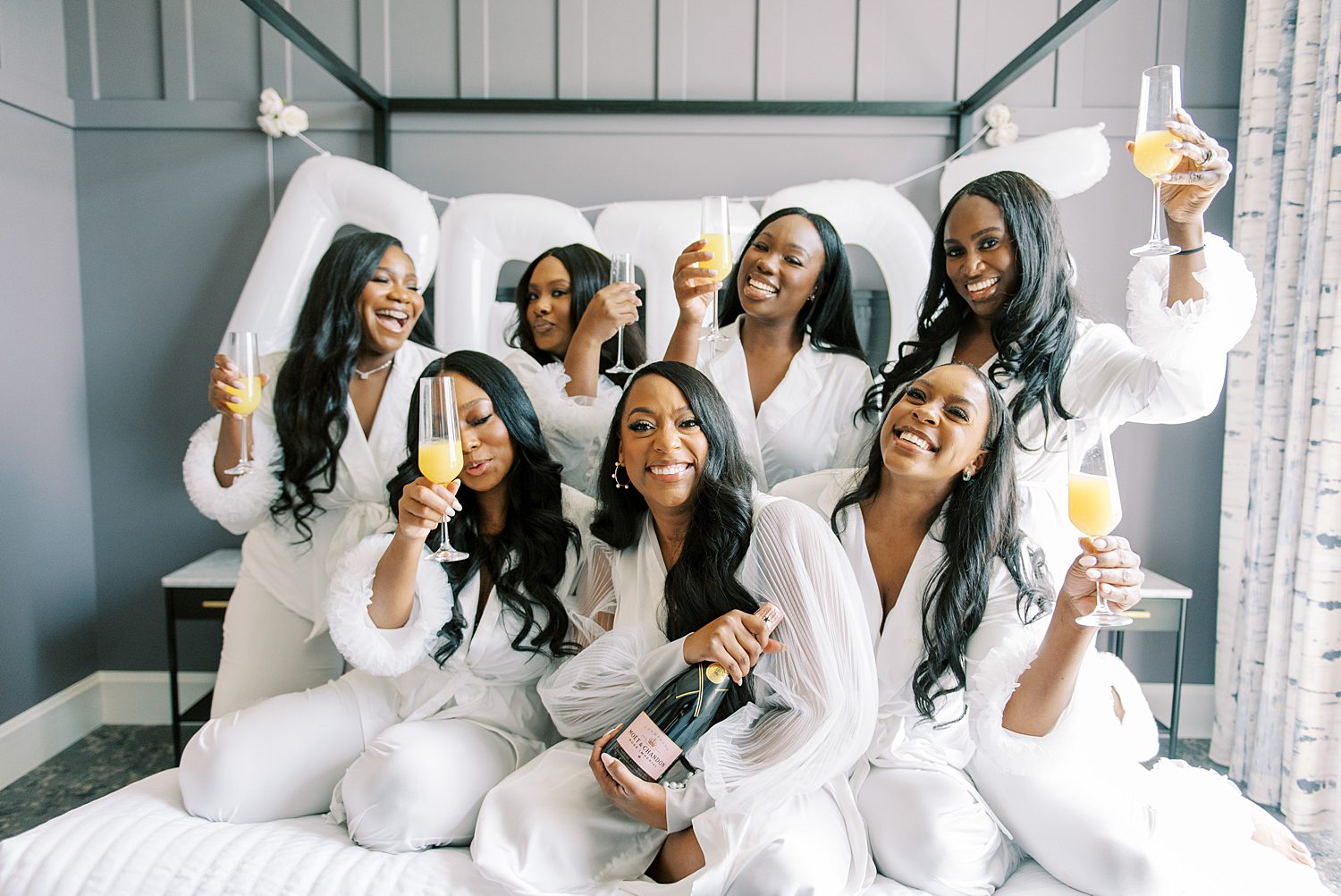 bridesmaids in white robes and pajamas toast with champagne and mimosas 