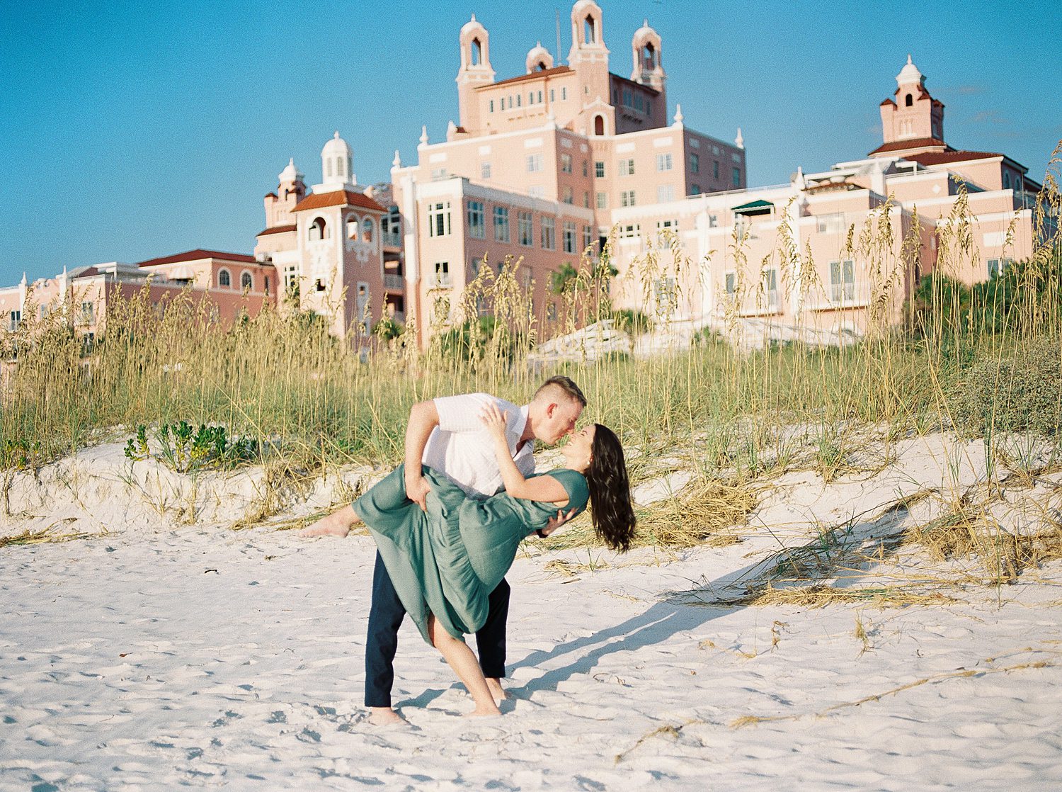 groom dips bride in green dress outside The Don Cesar Hotel during engagement session