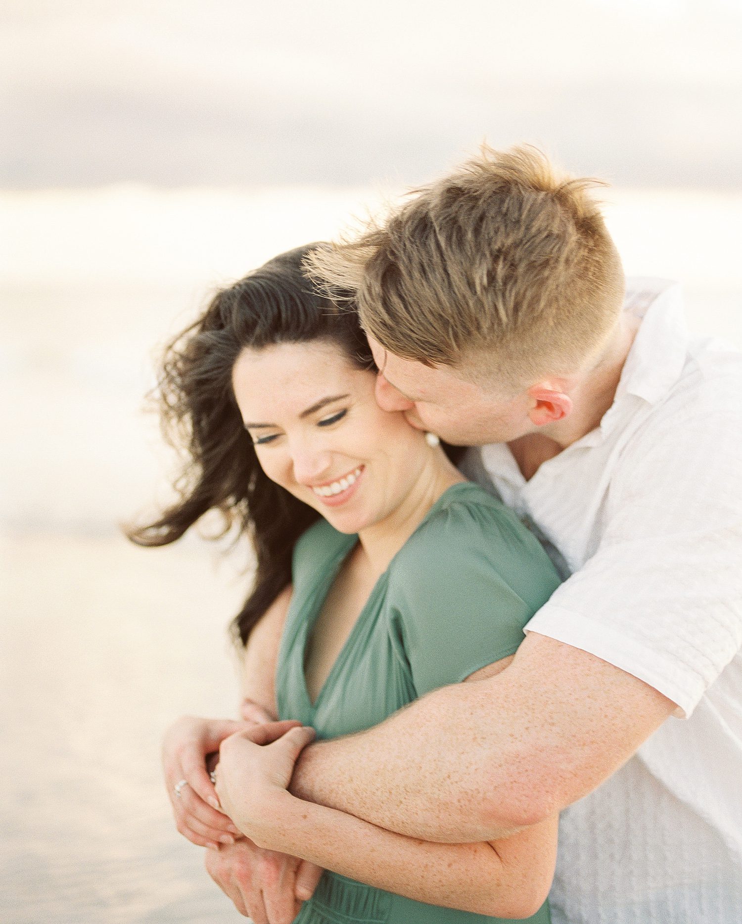 man hugs woman from behind during engagement session Tampa beach