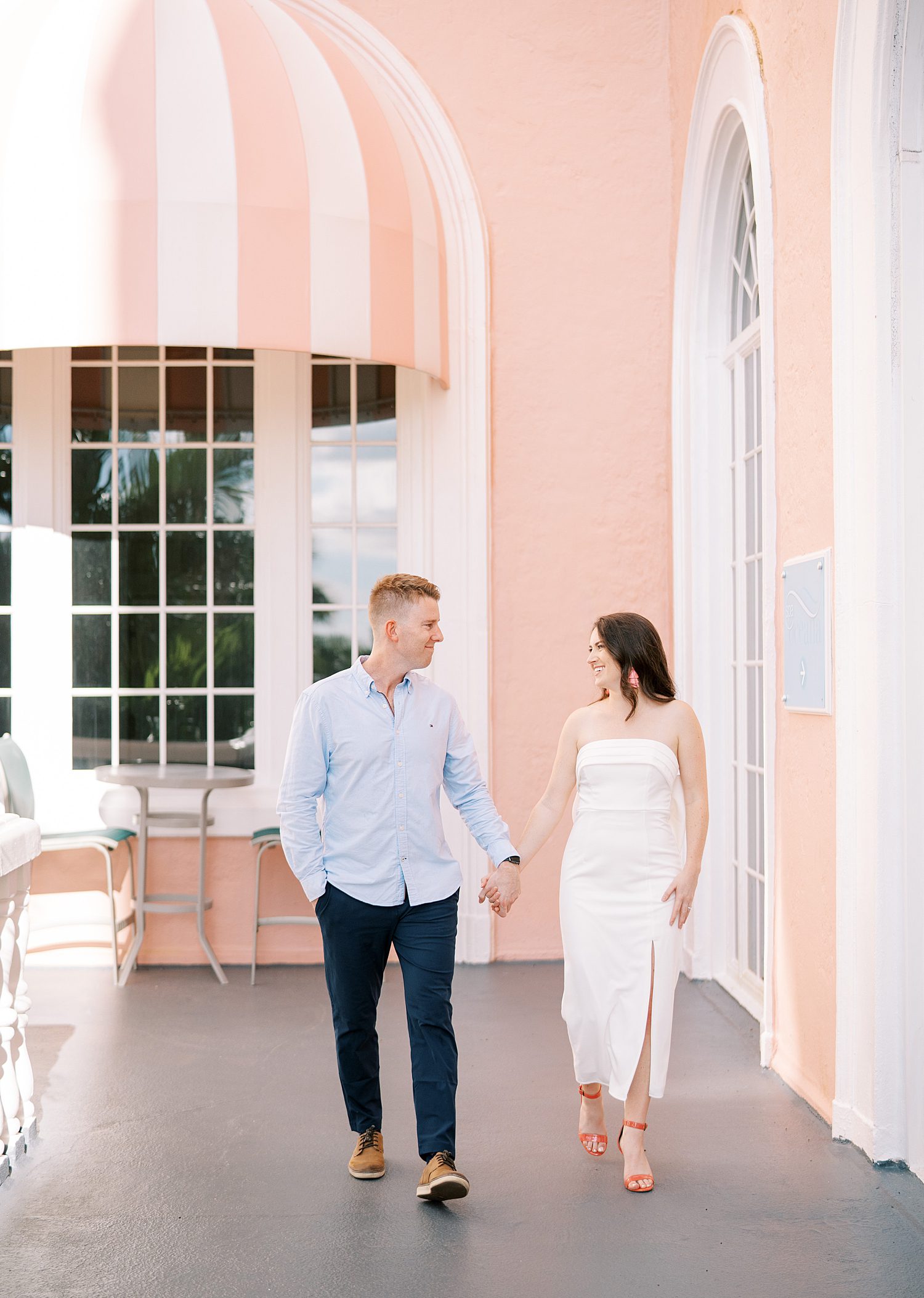 engaged couple holds hands walking down pink hallway at Don Cesar Hotel