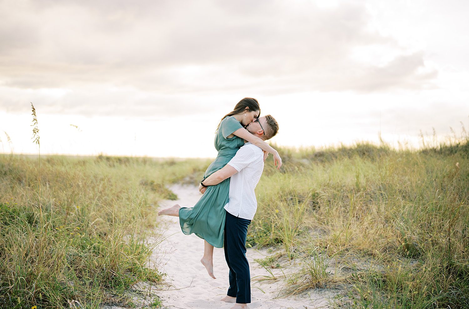 man lifts up fiancee in green dress on Tampa beach 