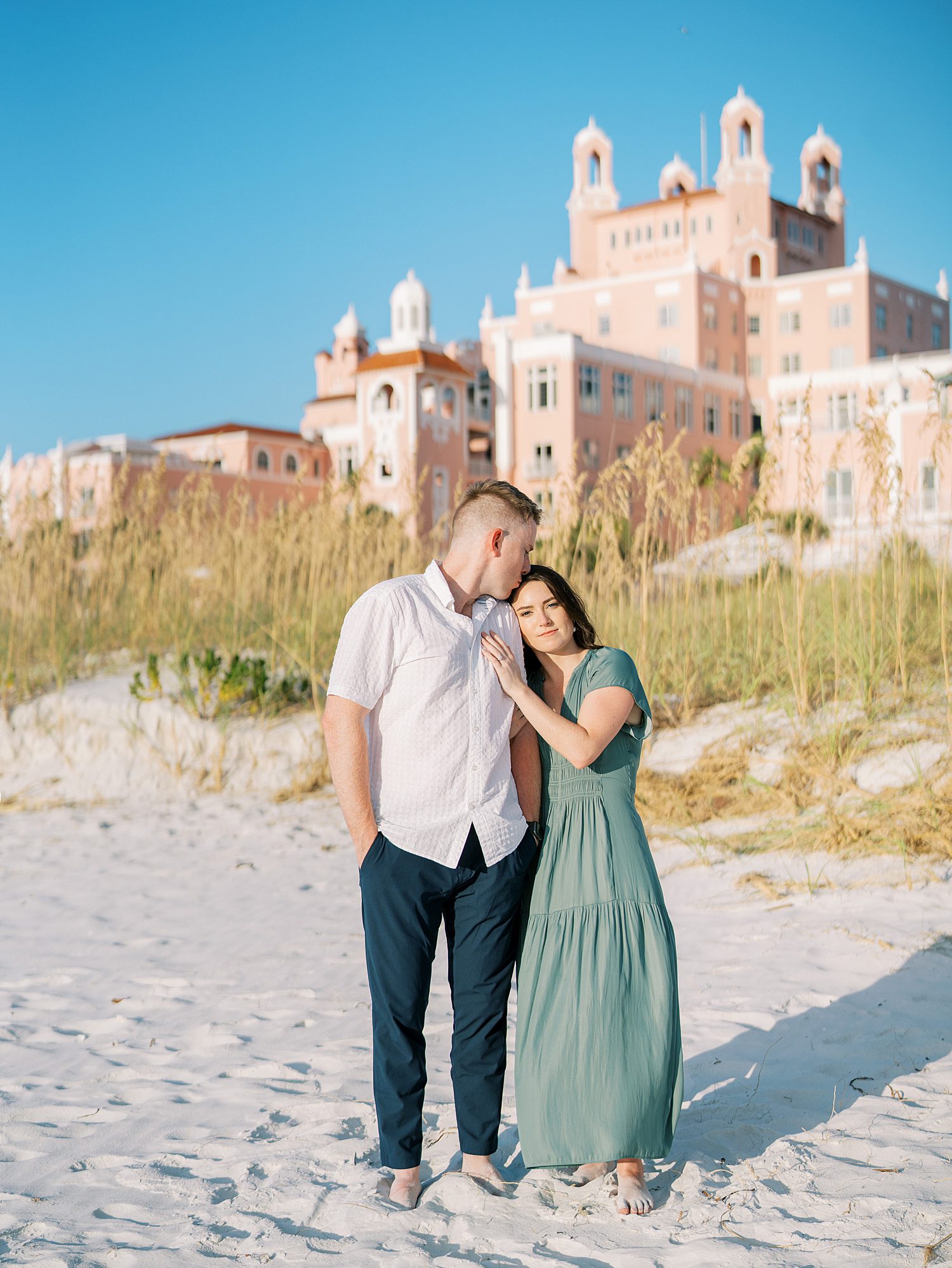 woman leans head on man's shoulder with the Don Cesar Hotel behind them on beach