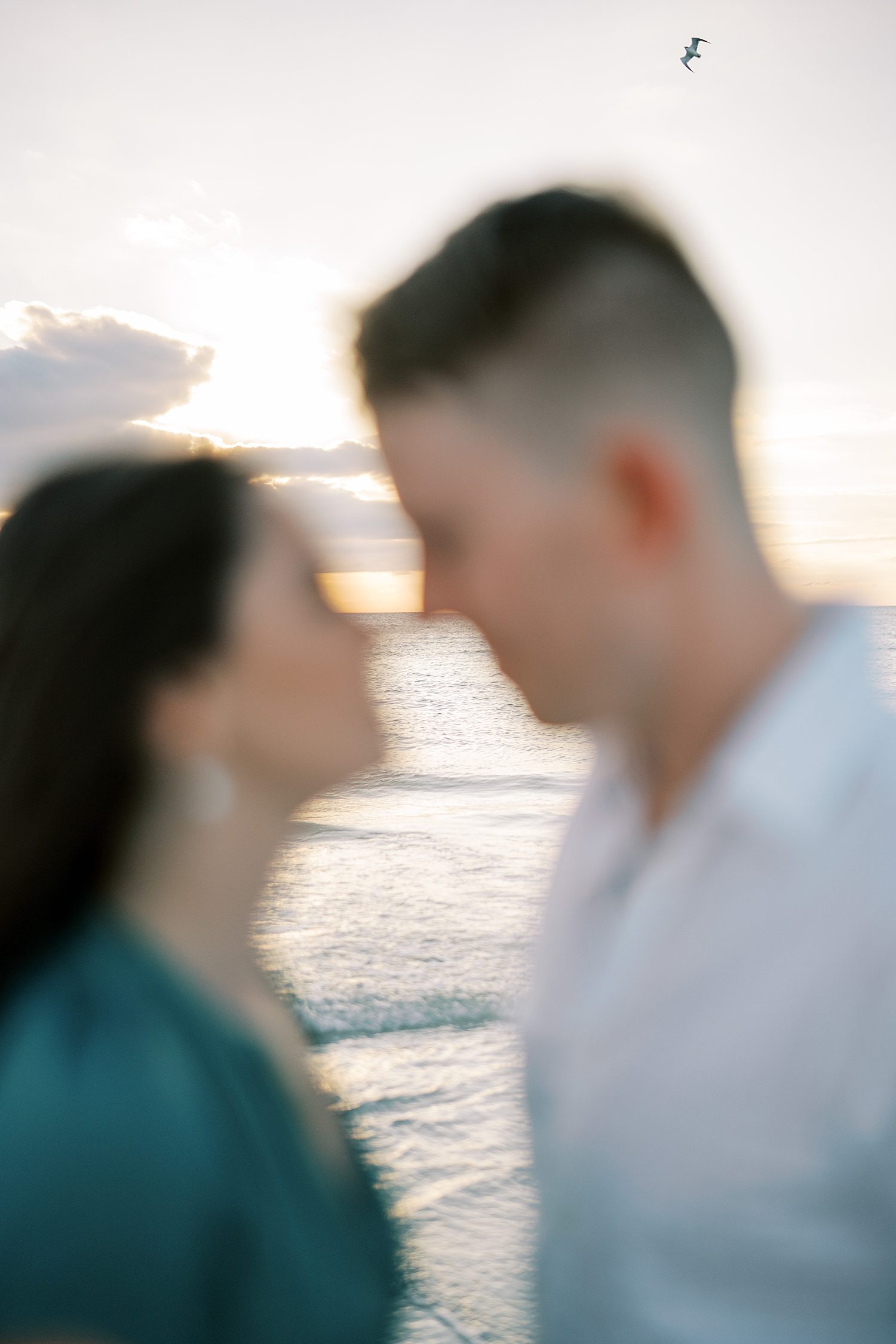 couple touches noses together blurred in front of ocean