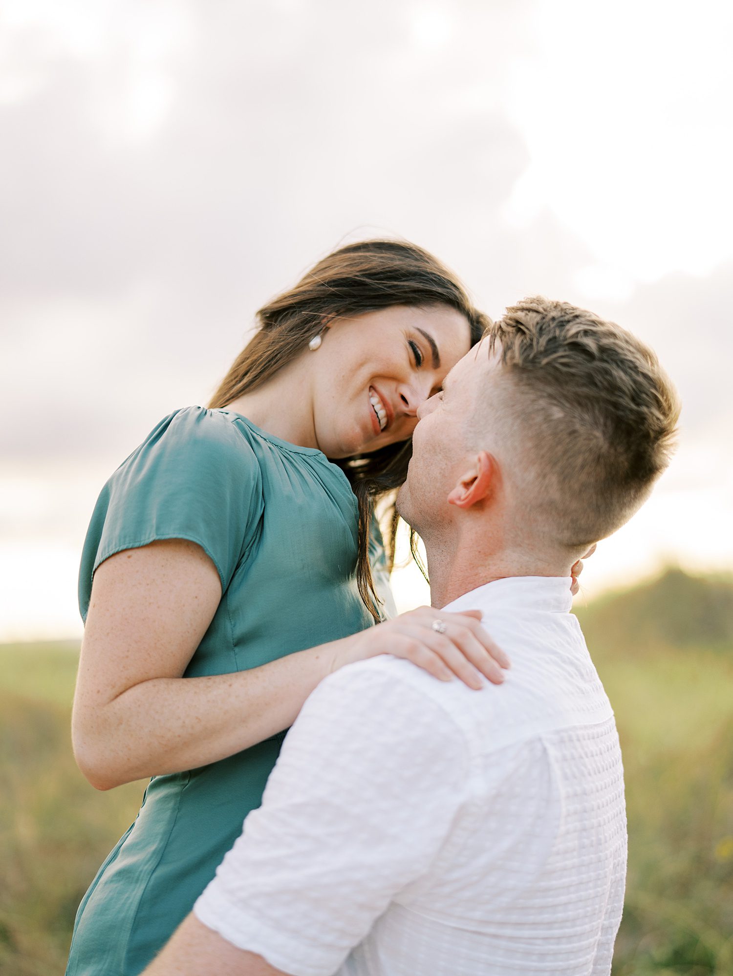 woman leans head while looking down at fiancee holding her in the air 