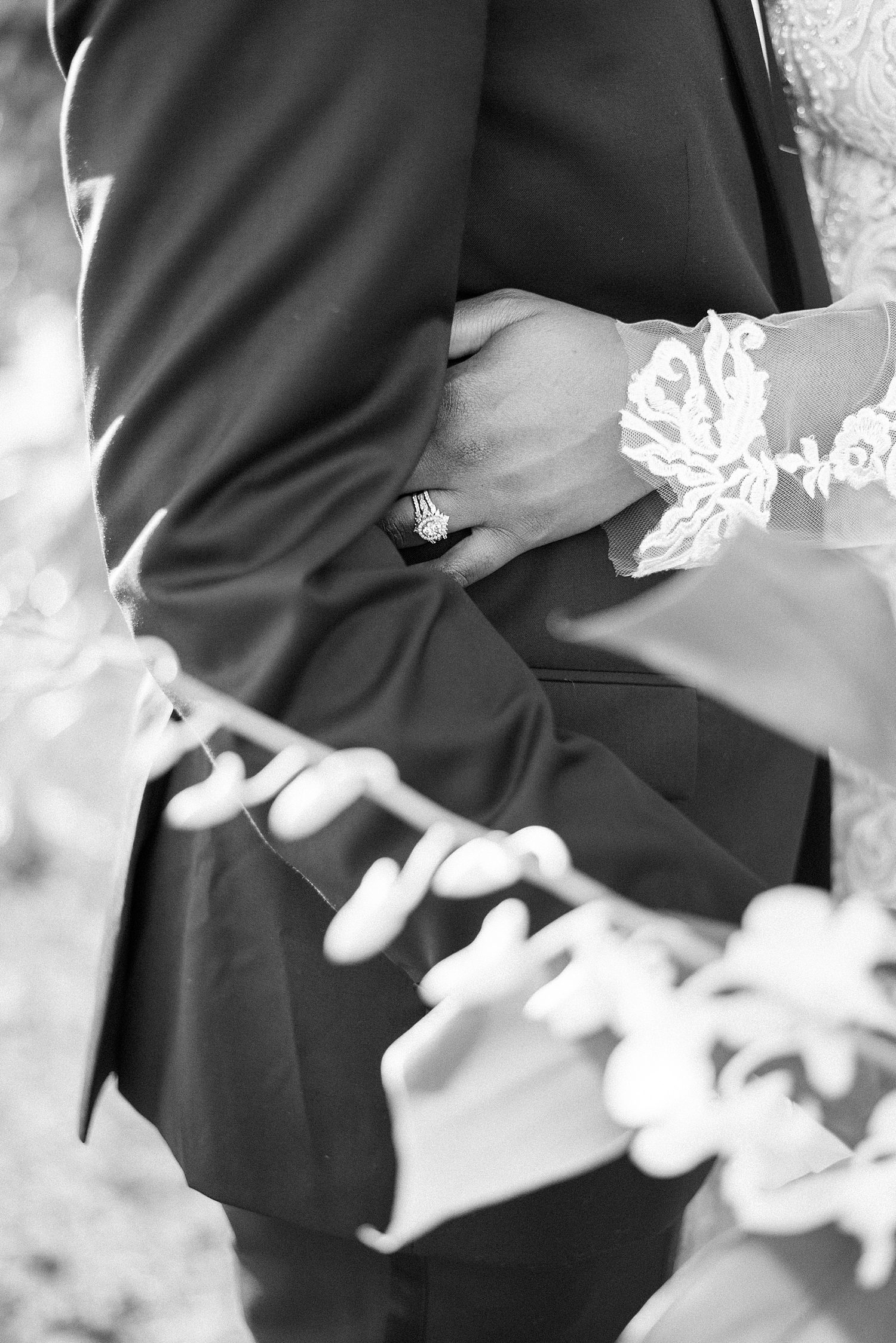black and white photo of bride hugging groom with lace of wedding dress sleeve near her wrist 