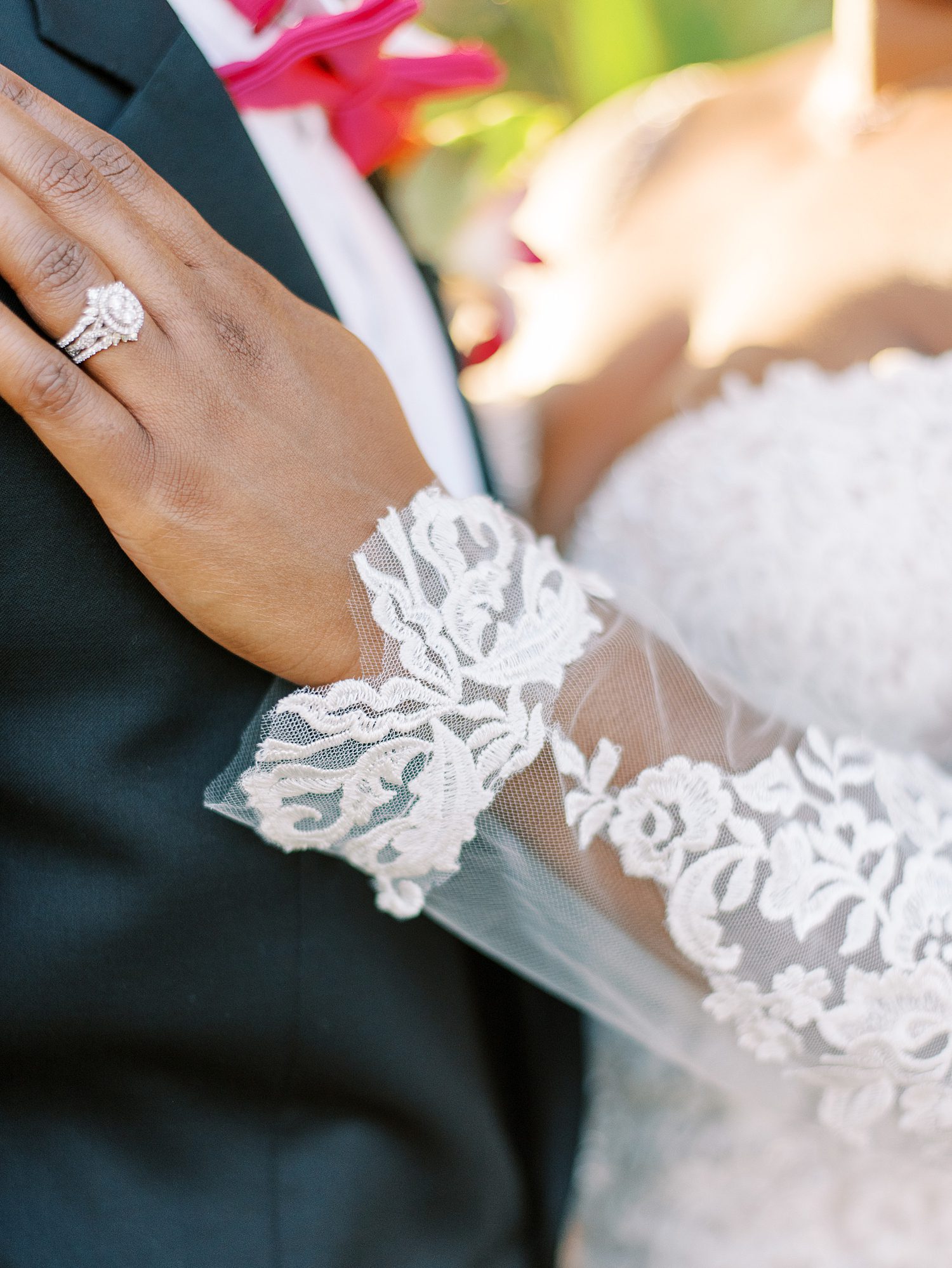 bride shows off engagement ring and lace of wedding dress sleeve on groom's chest