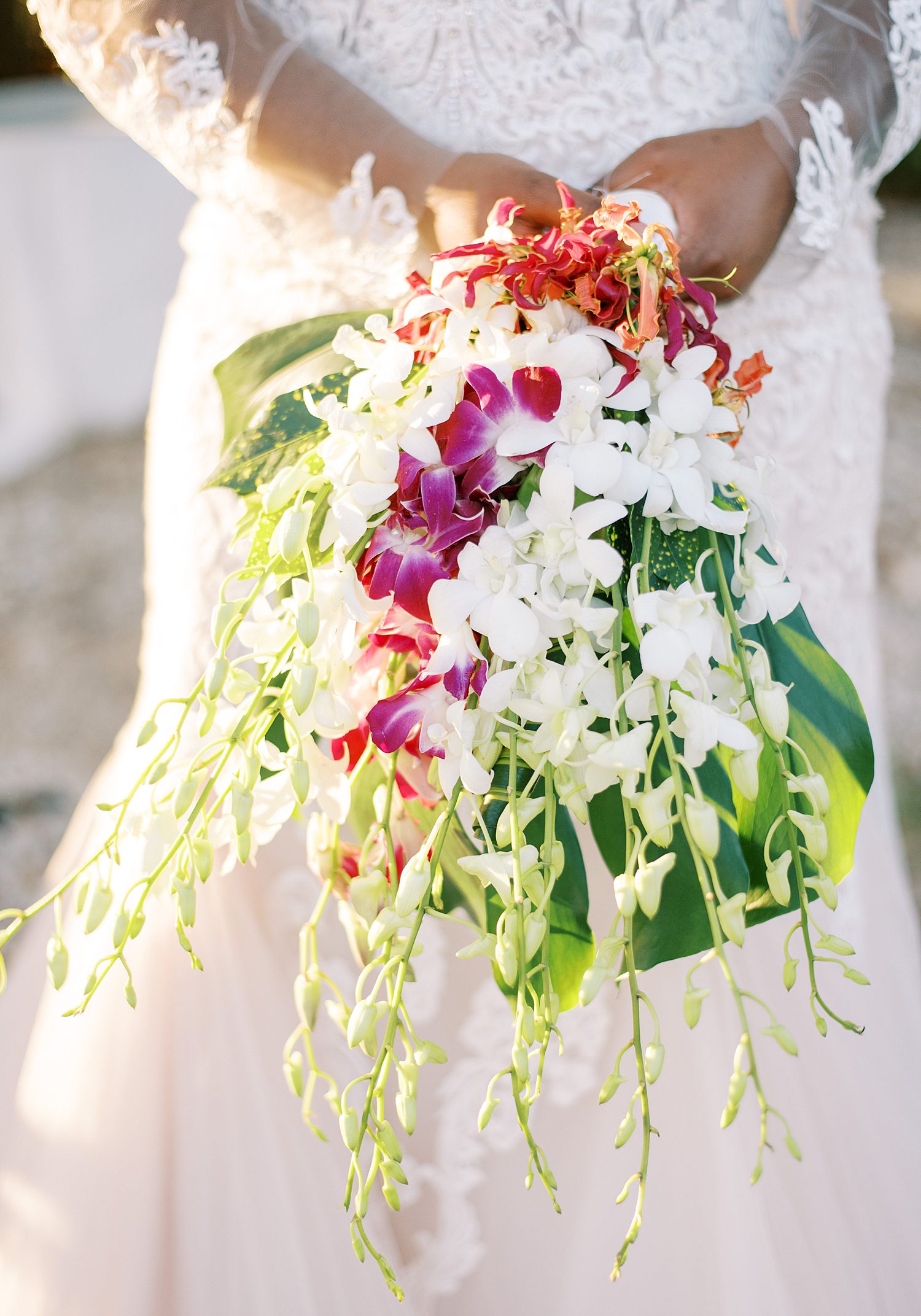 bride holds cascading tropical bouquet of purple and white flowers 