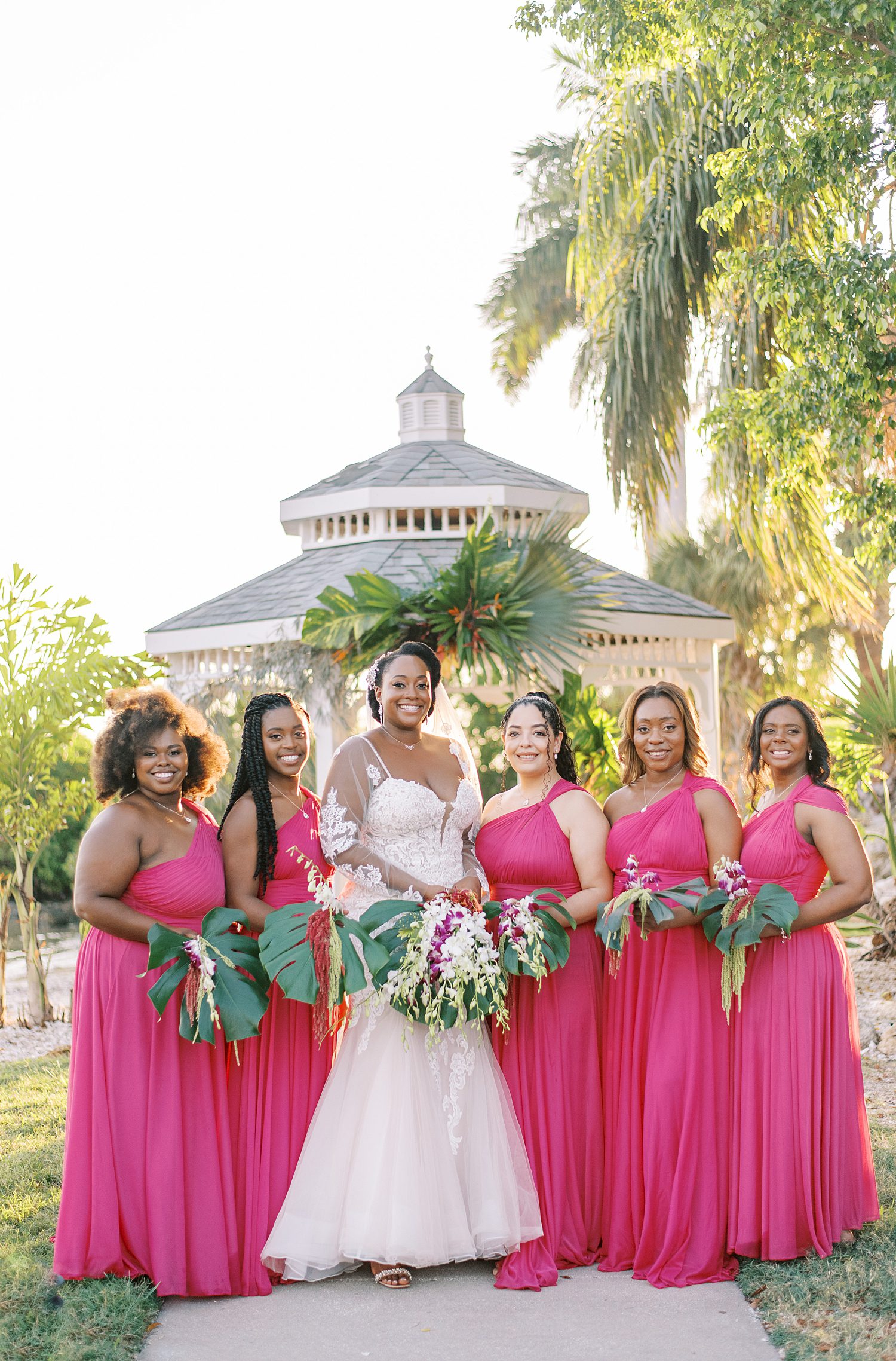 bride poses with bridesmaids in hot pink gowns with tropical bouquets at The Rusty Pelican Tampa