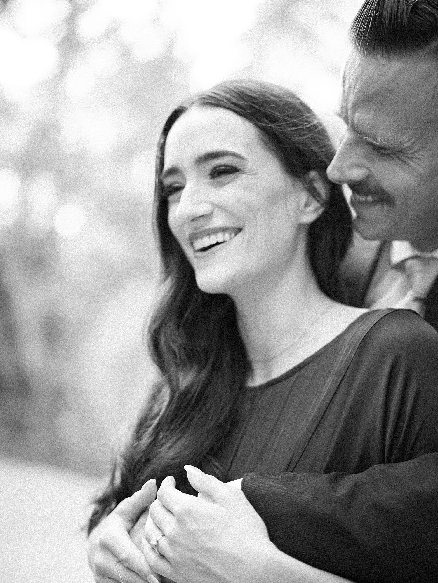 man hugs woman from behind making her smile during Tampa FL engagement photos