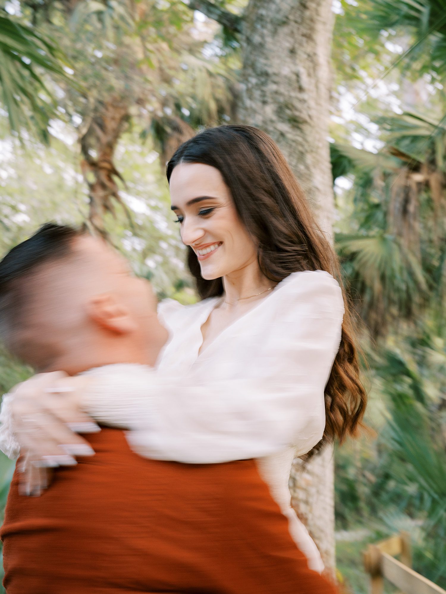 man in orange jacket lifts up fiancee in white dress