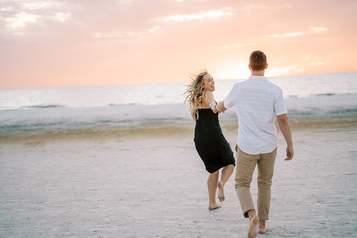 couple holds hands running down beach at sunset during Tampa FL engagement photos 