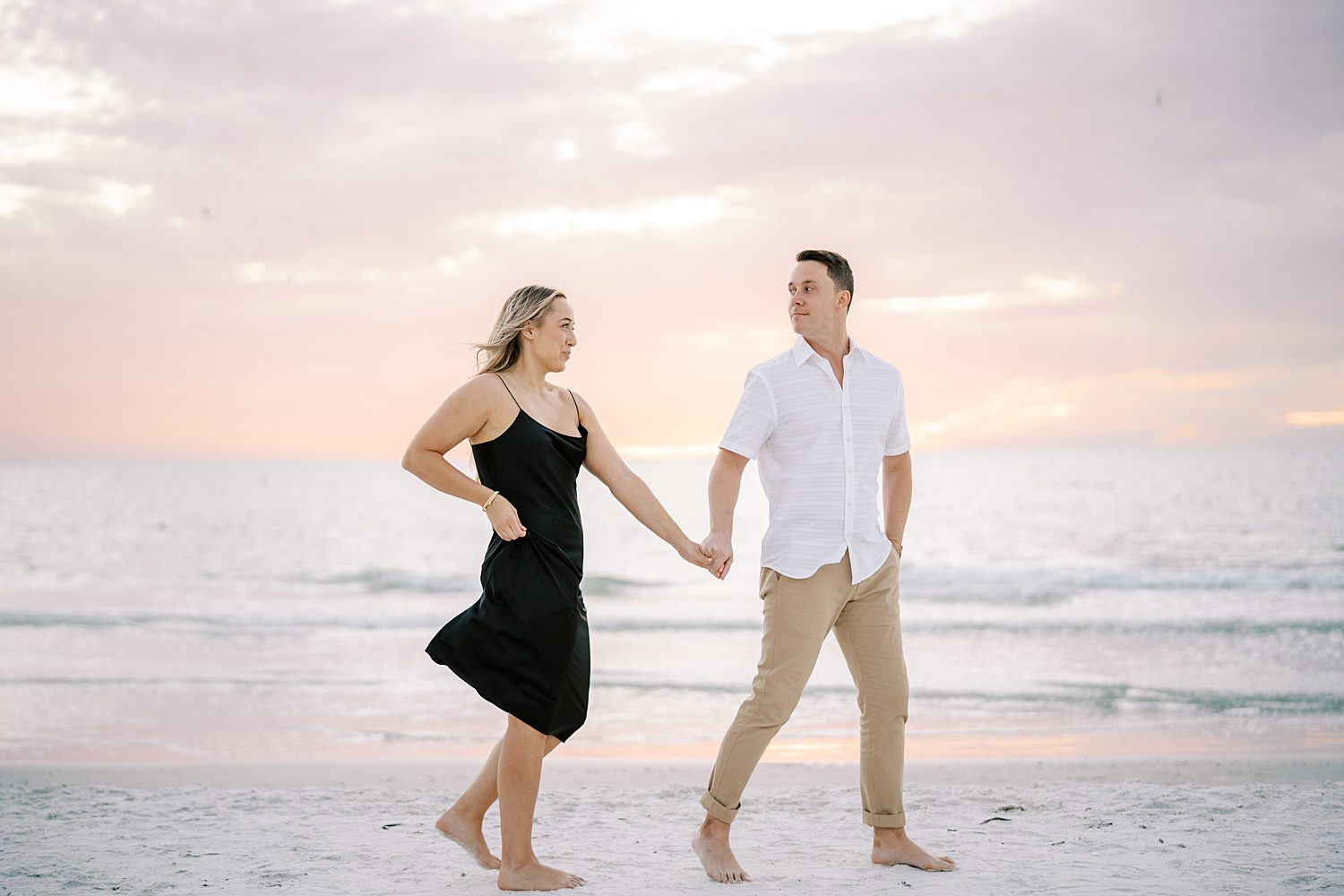 couple holds hands walking on beach at sunset in Florida 