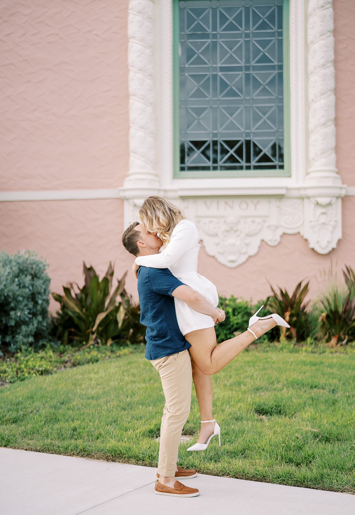 man lifts up fiancee in front of pink and white building in Tampa FL