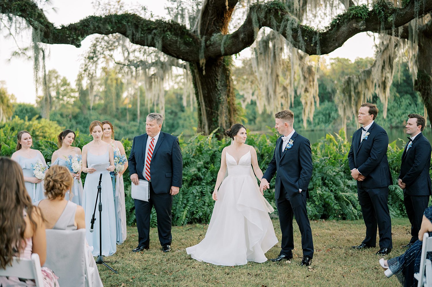 bride and groom hold hands walking down aisle at open air reception at Innisbrook Resort in front of tree with Spanish moss