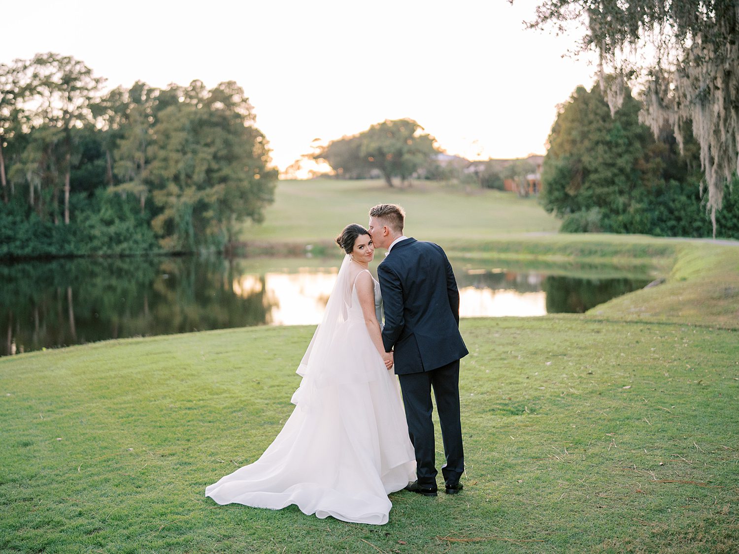 groom leans to kiss bride's cheek in front of pond at Innisbrook Resort
