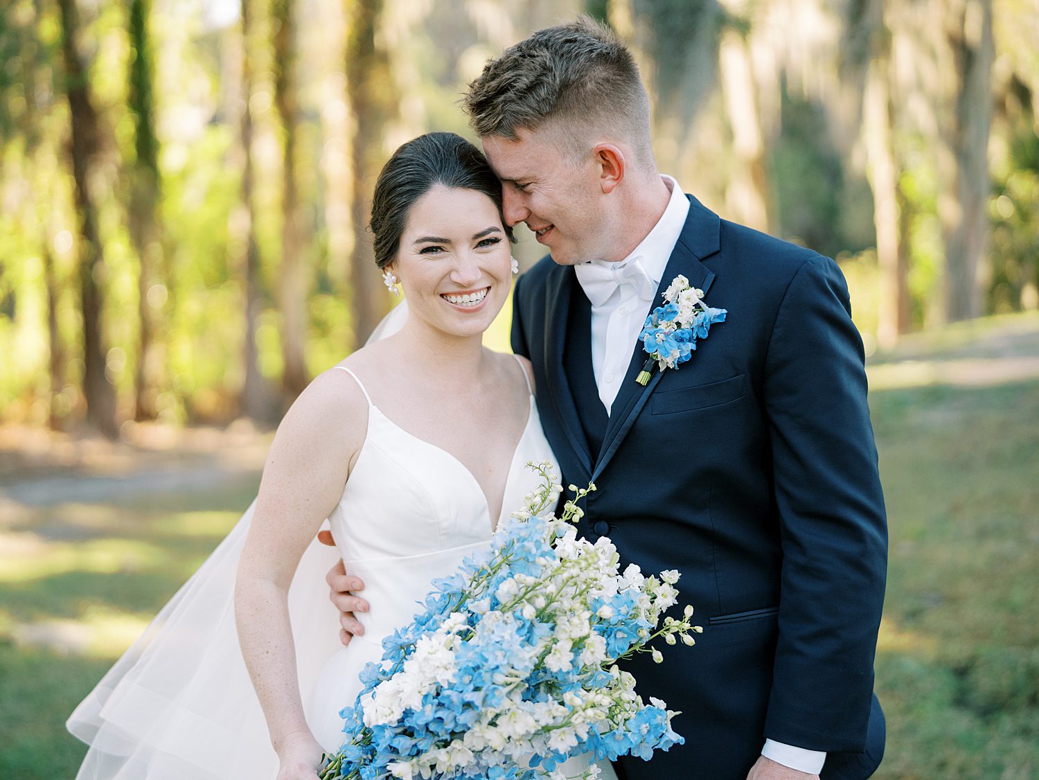 groom nuzzles bride's cheek as she holds blue and white bouquet