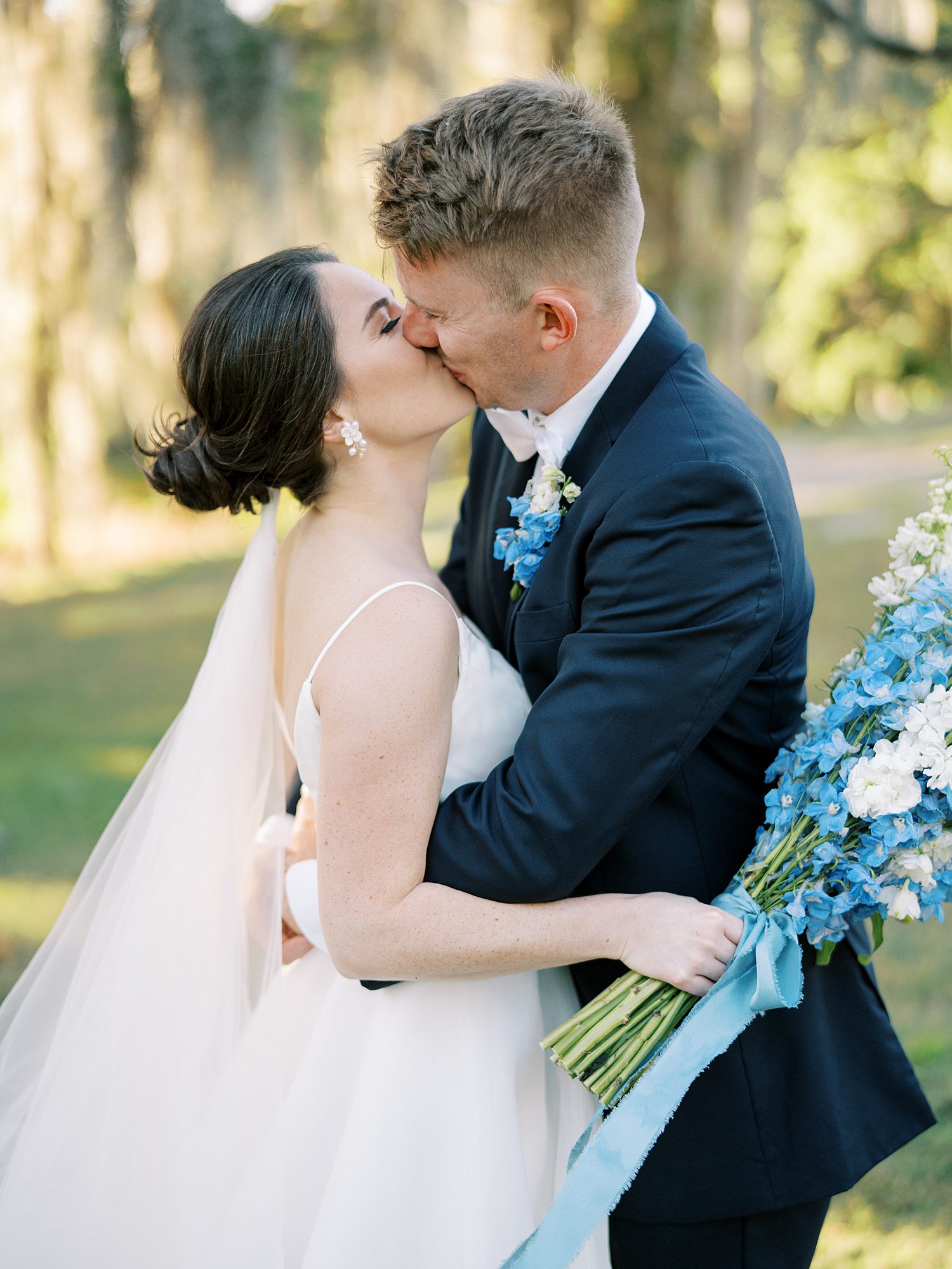 newlyweds kiss and bride holds bouquet of blue and white flowers at Tampa venue 