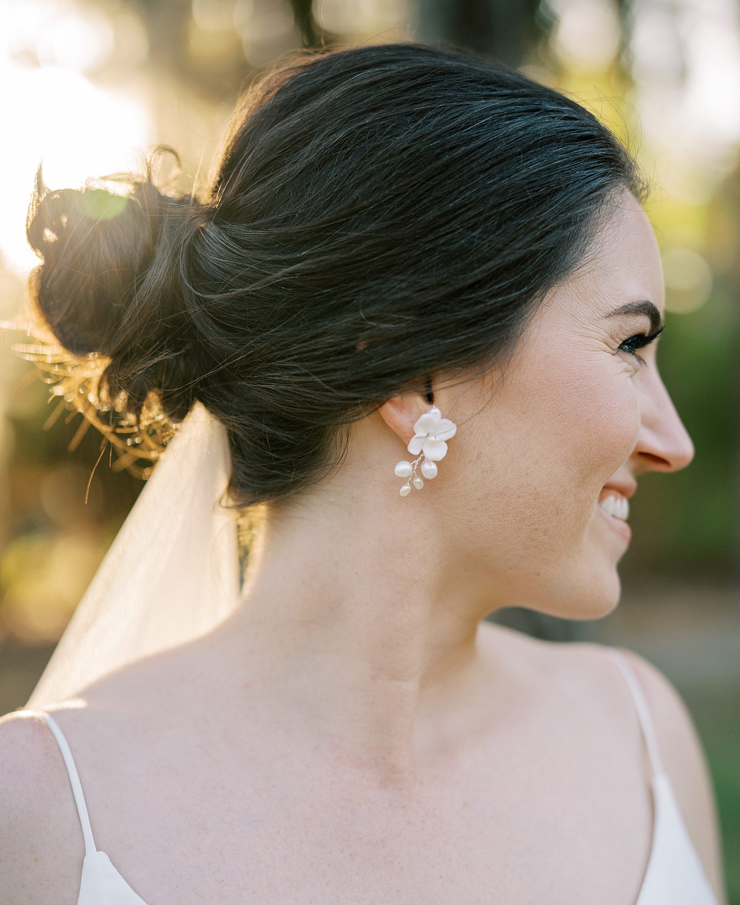 brunette bride smiles over shoulder showing off pearl flower earrings 
