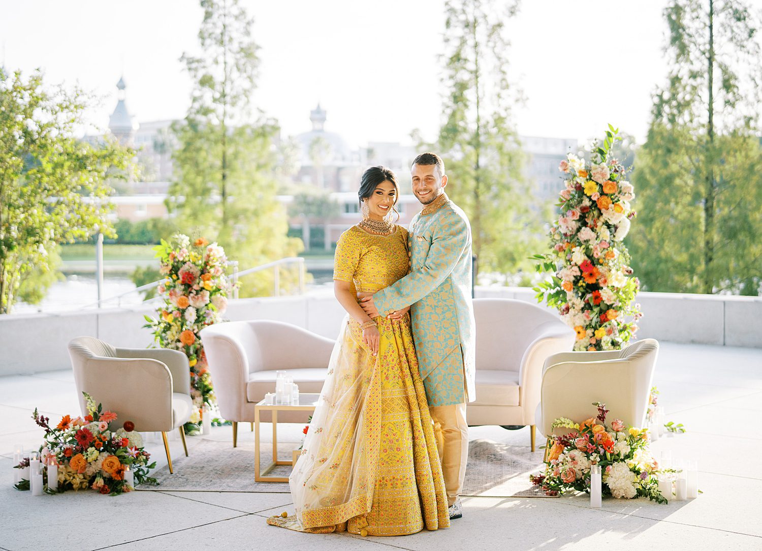 couple hugs in traditional green and gold attire on patio during Mehndi Day at the Tampa Museum of Art
