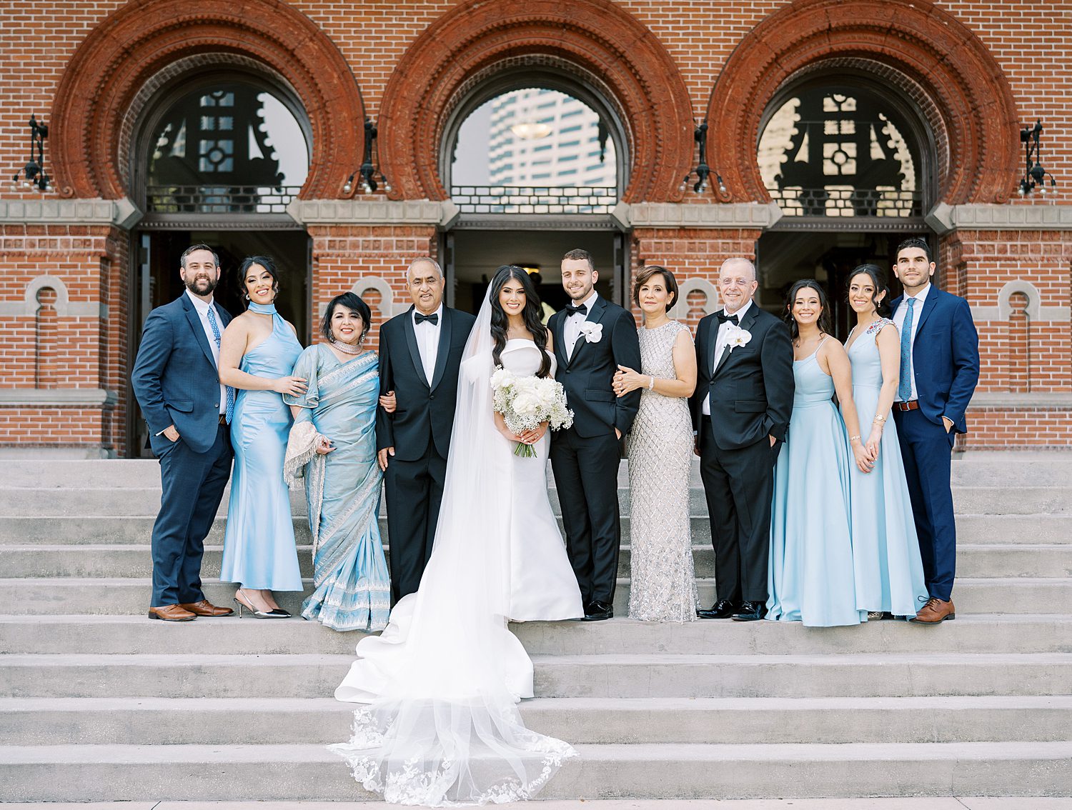 bride and groom stand on steps of Armature Works with bridesmaids and family