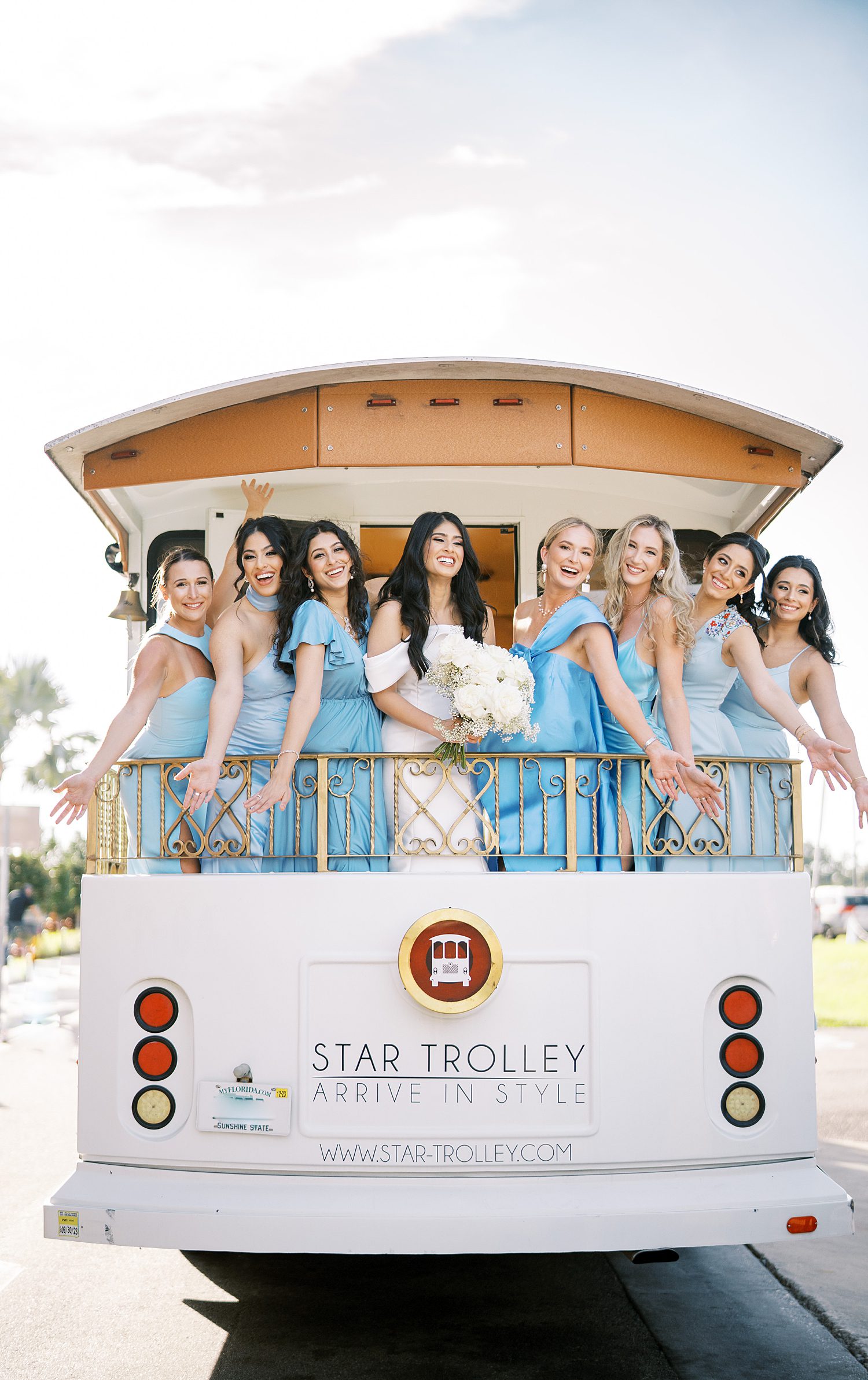 bride and bridesmaids in light blue gowns pose on back of trolley in Tampa FL