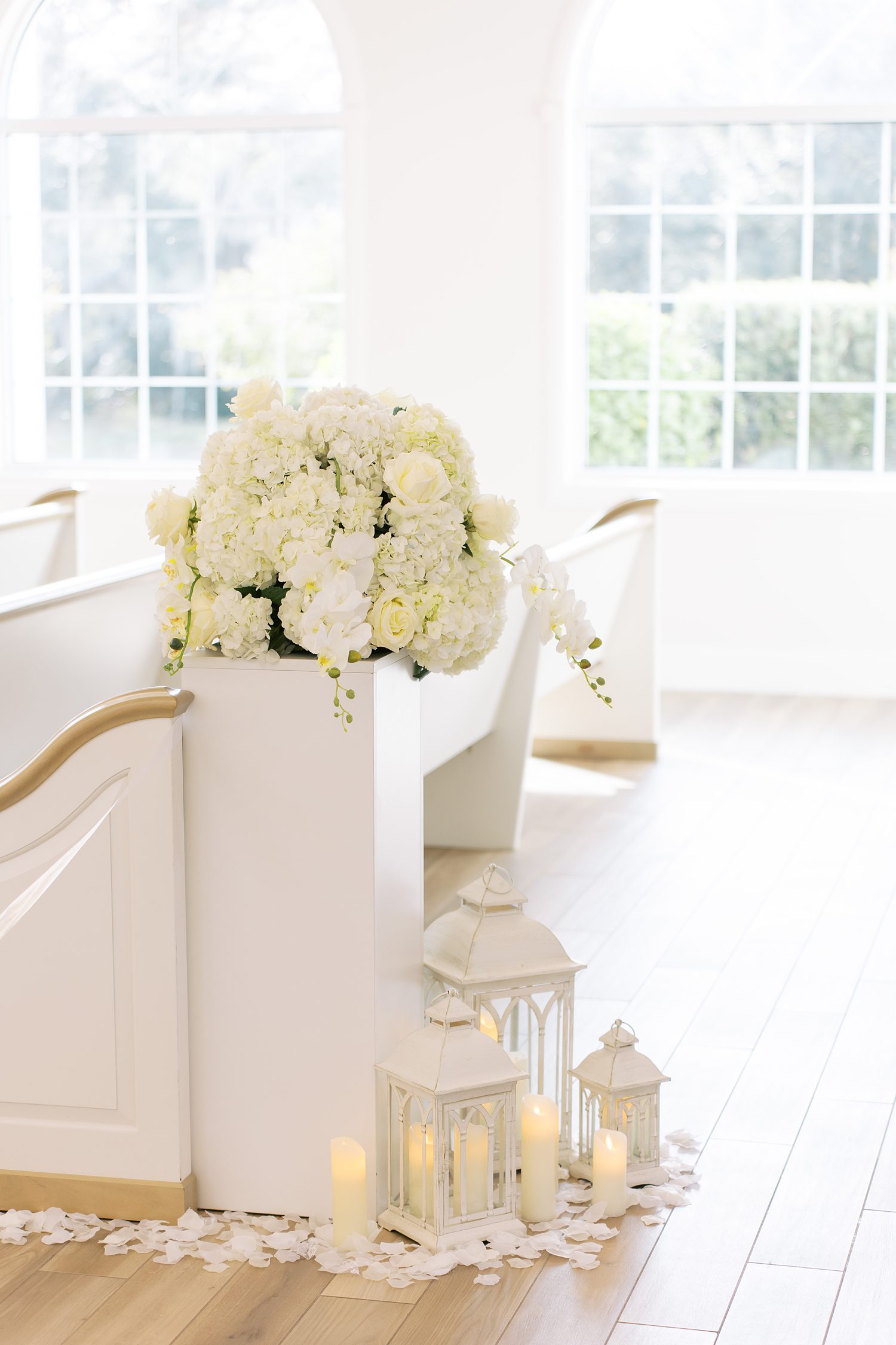 ivory flowers sit on pew next to white lanterns inside Harborside Chapel
