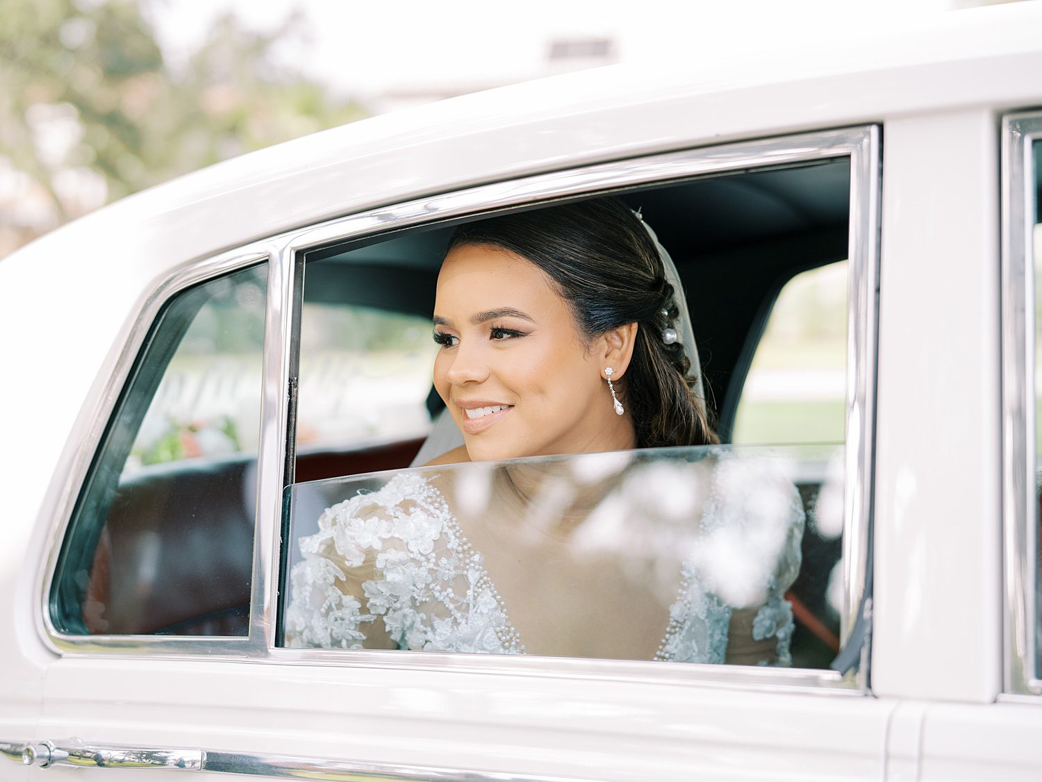bride looks out the window of vintage white car on wedding morning 