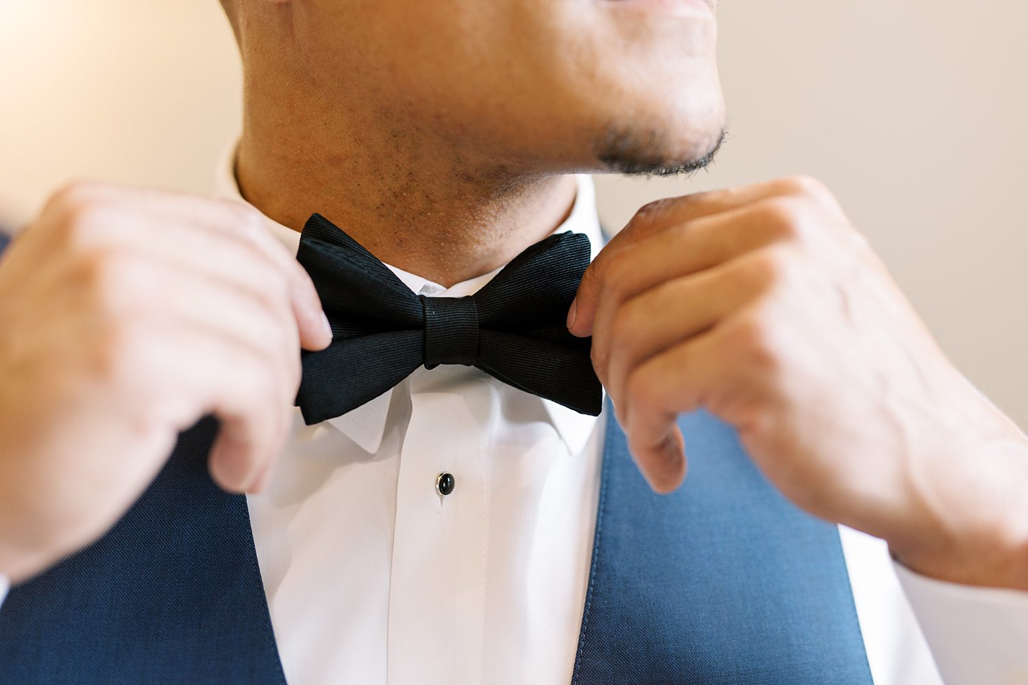 groom adjusts black tie above navy suit vest before Tampa FL wedding day