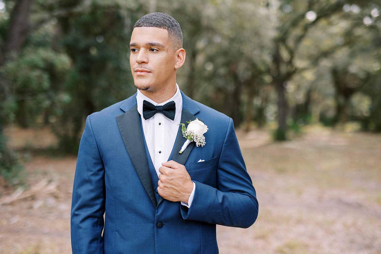 groom in navy suit with black lapels holds jacket