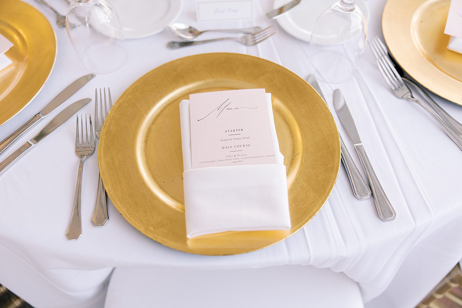 wedding reception place setting with gold charger on white table cloth 