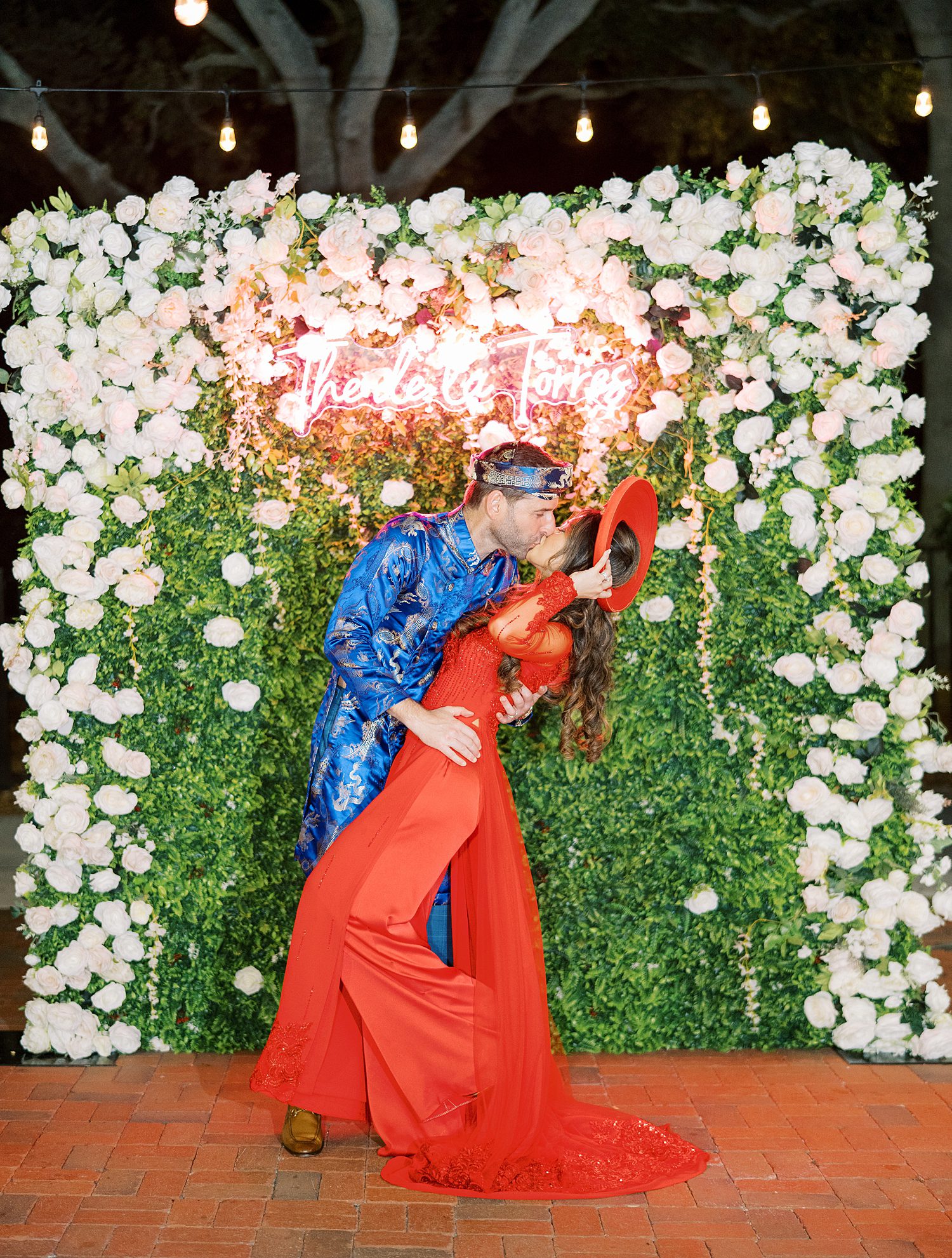bride and groom kiss in  traditional Vietnamese wedding attire in front of flower wall in Tampa Yacht Club