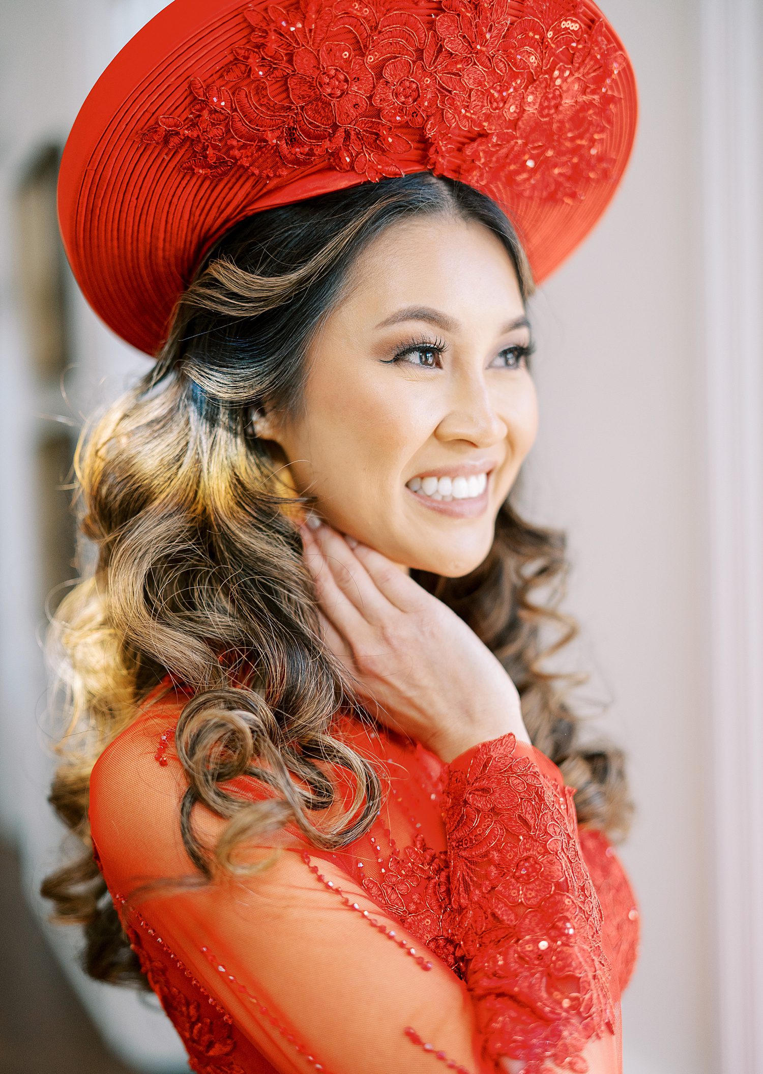 bride holds neck wearing traditional red Vietnamese dress and hat 