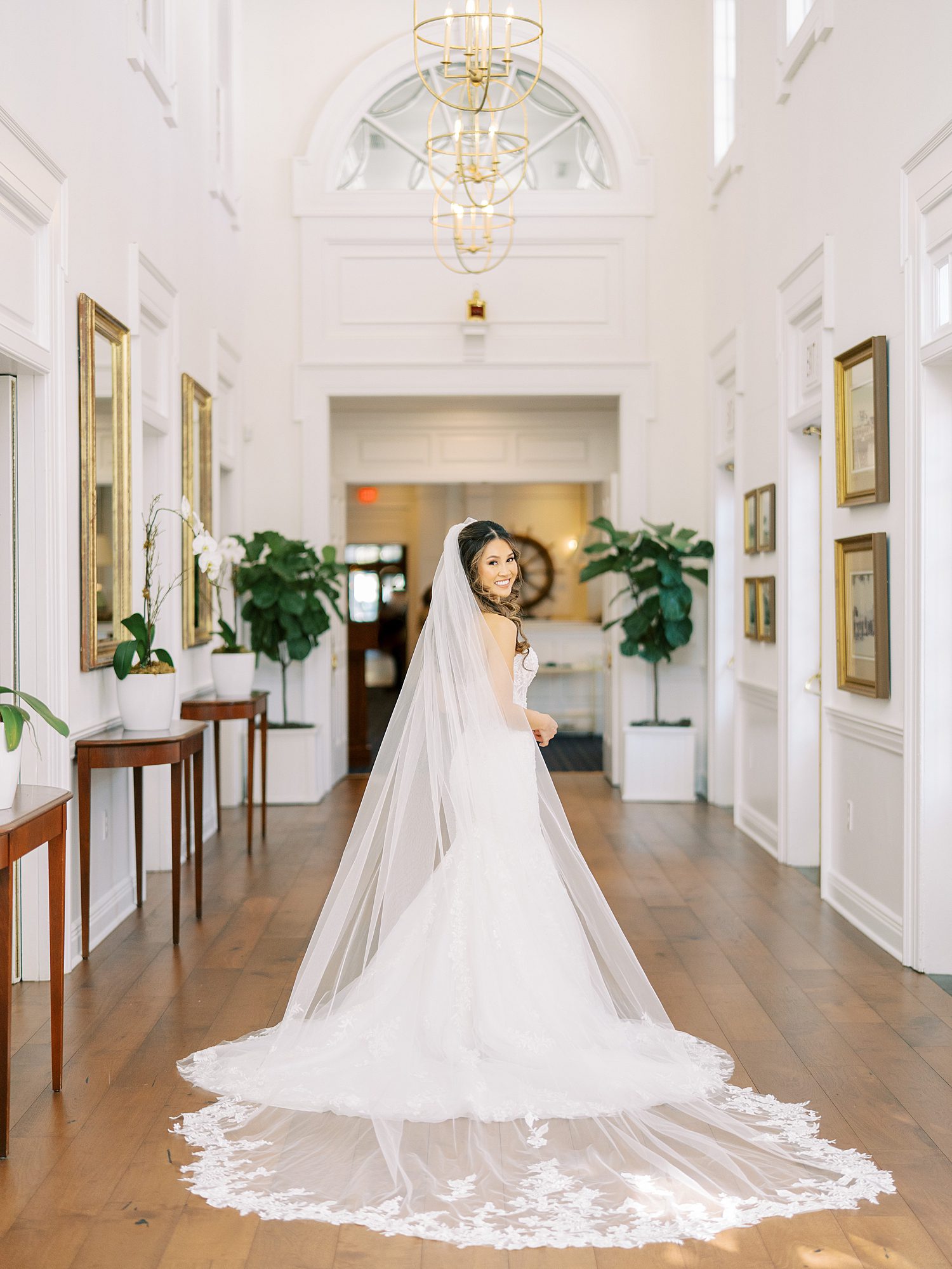 bride looks over shoulder in wedding gown with veil draped behind her in hallway at Tampa Yacht Club