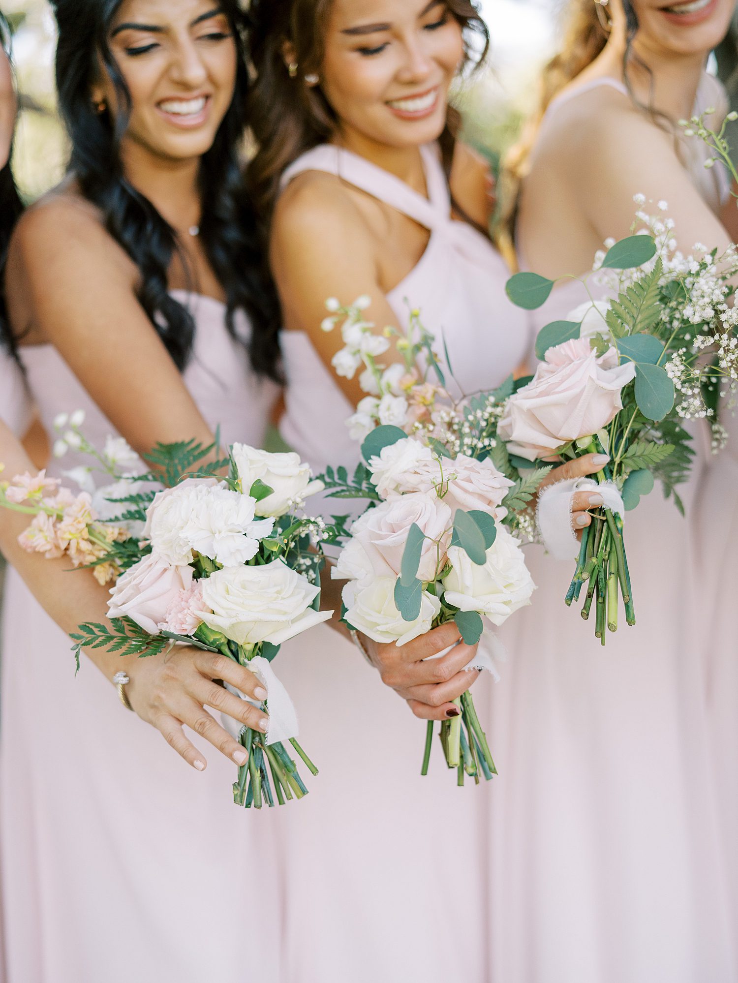 bridesmaids in blush gowns hold bouquet of white and pink flowers 