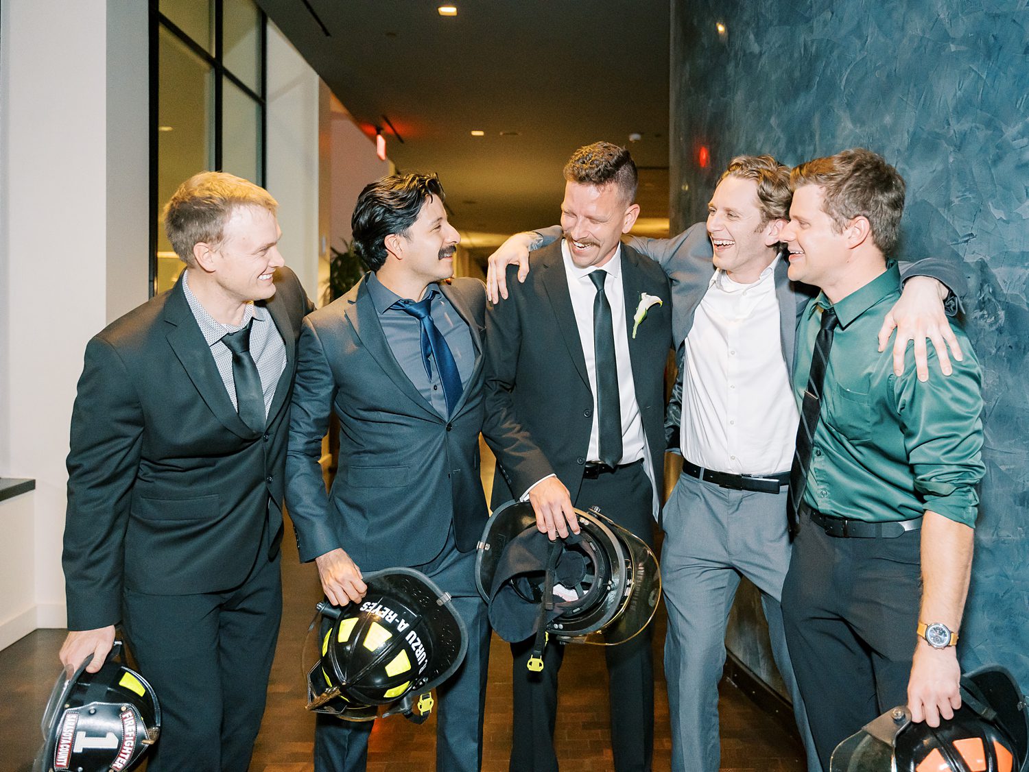 groom smiles hugging groomsmen with fireman's hat 