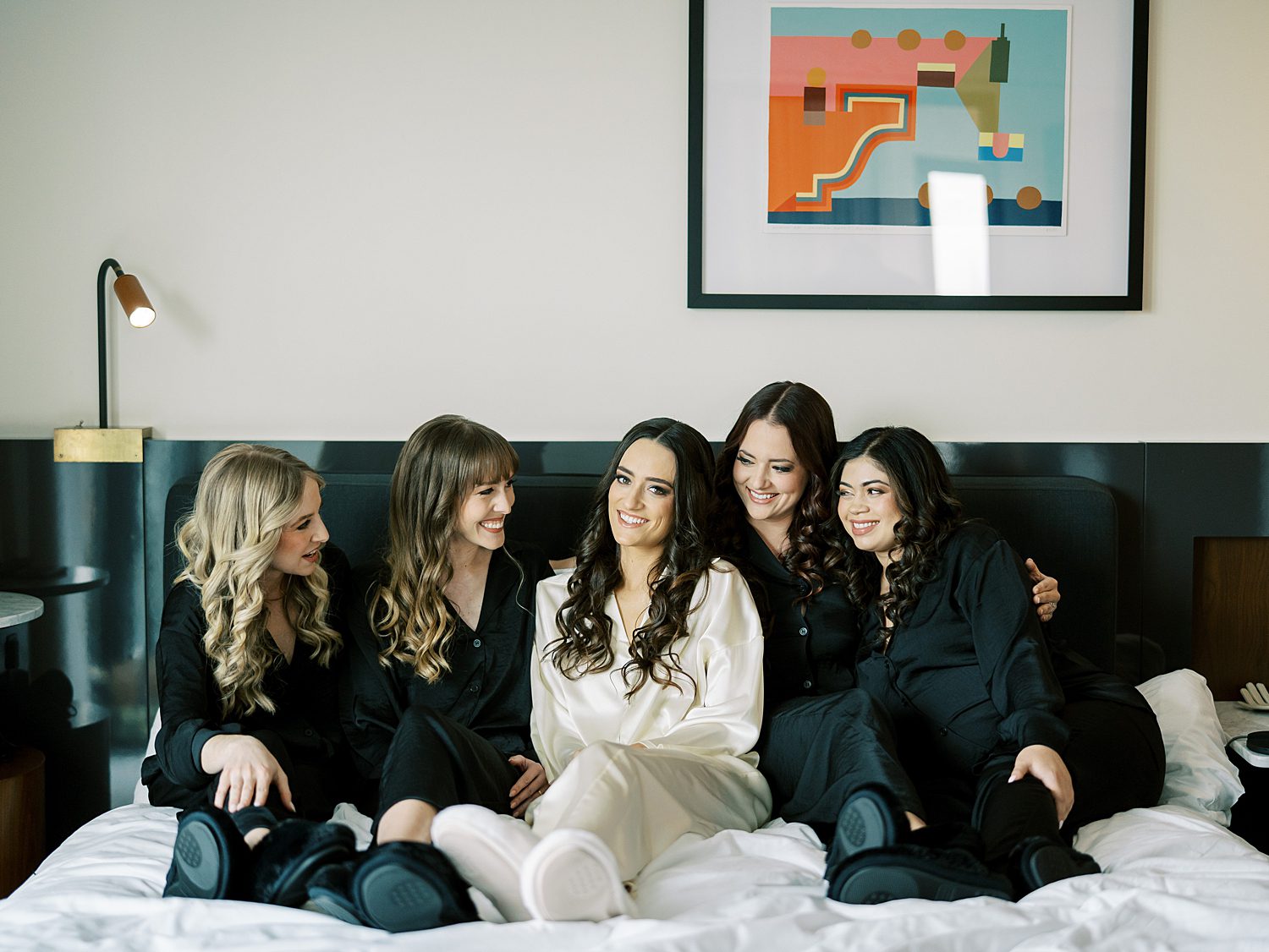 bride sits on bed at the Hotel Haya with bridesmaids in black pajamas 