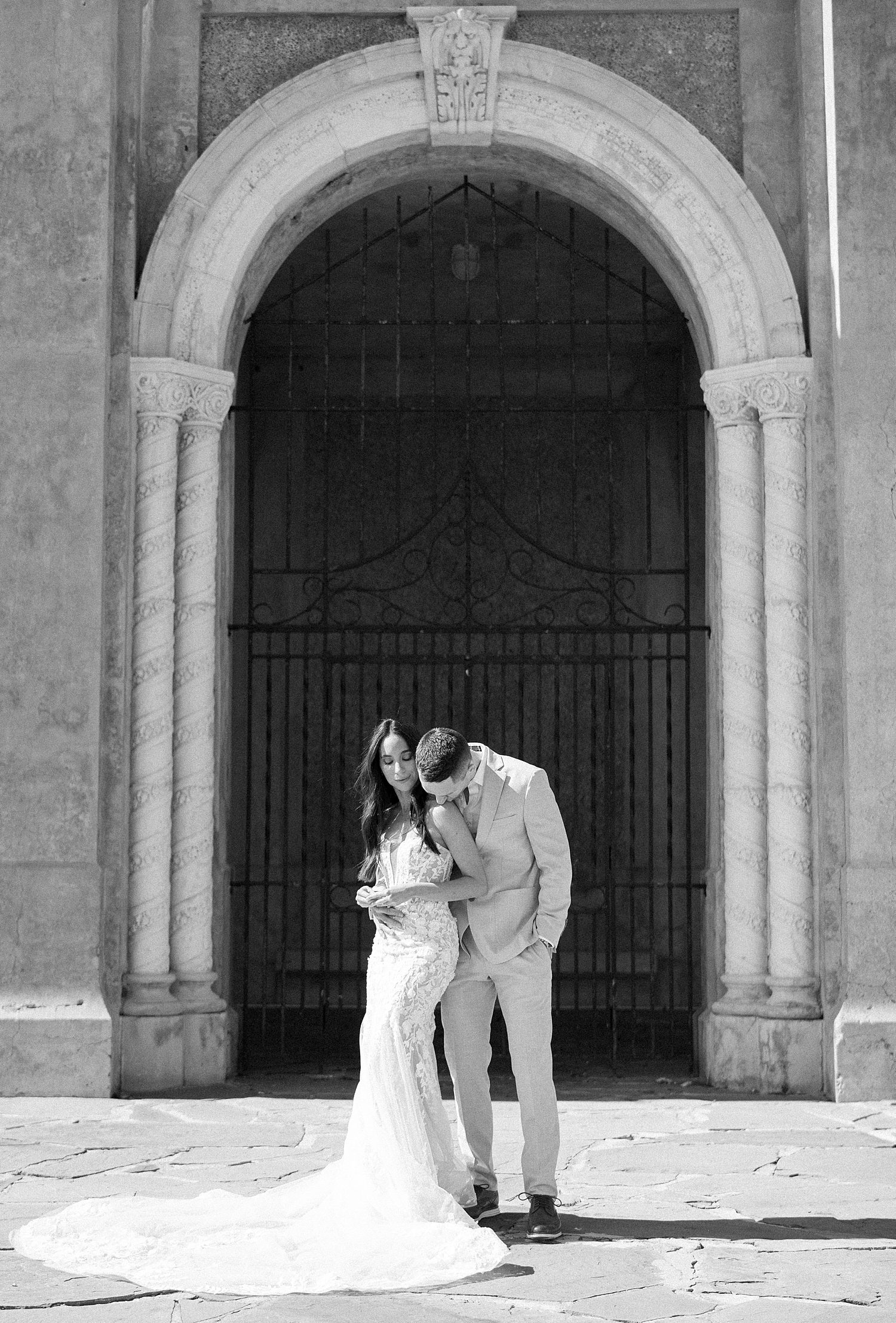 man leans to kiss woman's shoulder in front of gate at Hollis Gardens