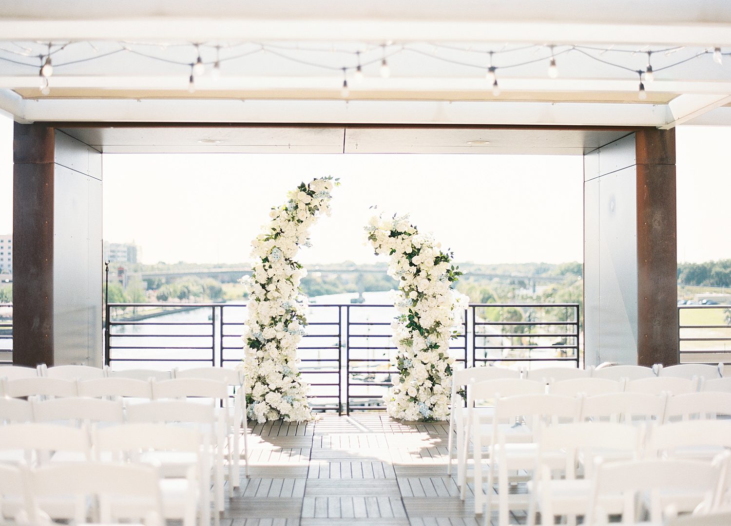 wedding floral arches at end of aisle lined with white chairs at Armature Works