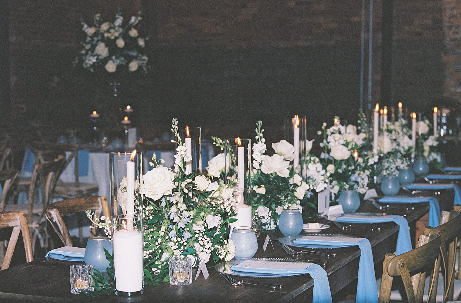 film photo of table with blue napkins, blue glasses, white taper candles, and white flowers