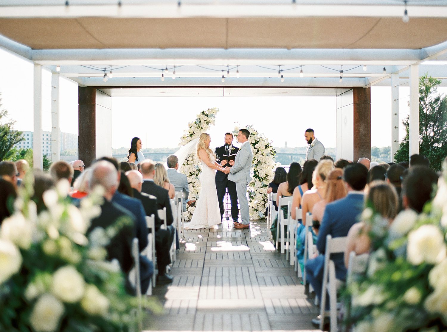newlyweds hold hands during wedding ceremony on rooftop of Armature Works
