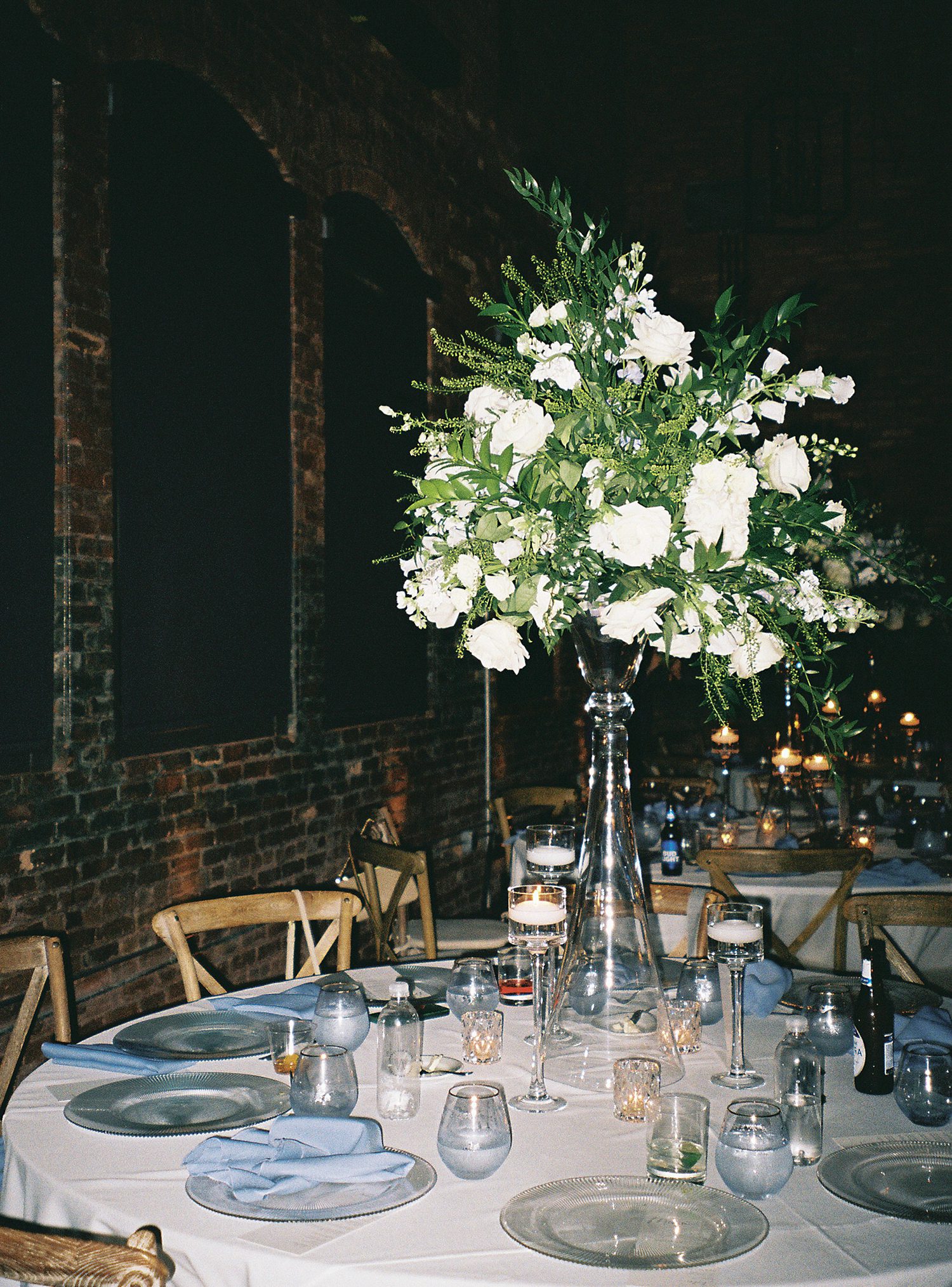 tall floral arrangement with white flowers on table with blue plates and napkins at Armature Works