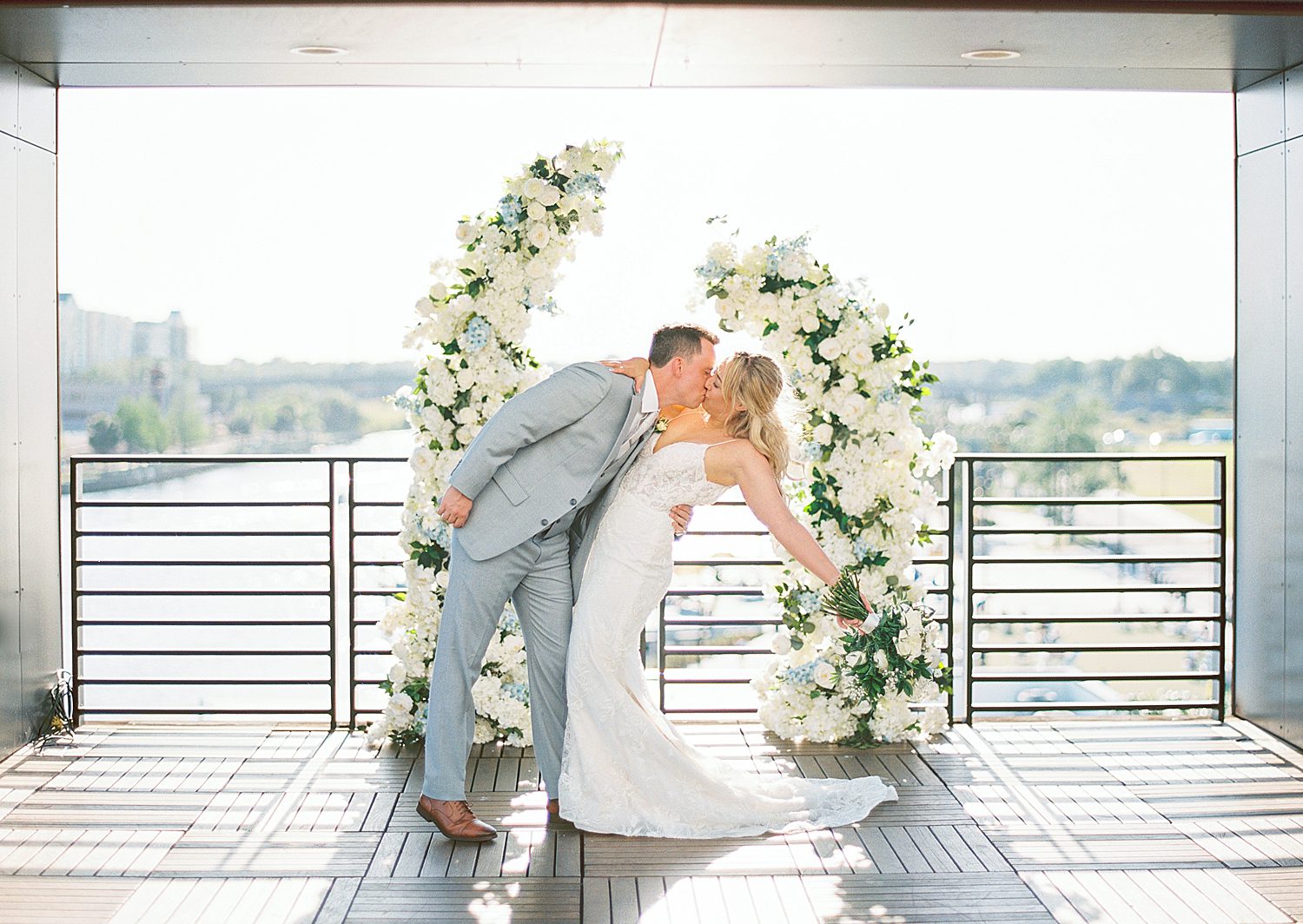bride and groom kiss by white floral arbor on rooftop in Tampa FL