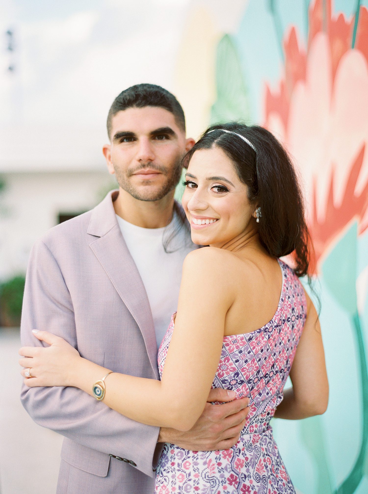 man in pink suit hugs bride to him by colorful mural at the Mayfair Hotel