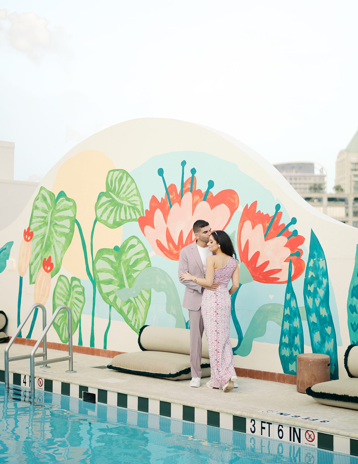 bride and groom hug by colorful floral mural by pool at the Mayfair Hotel