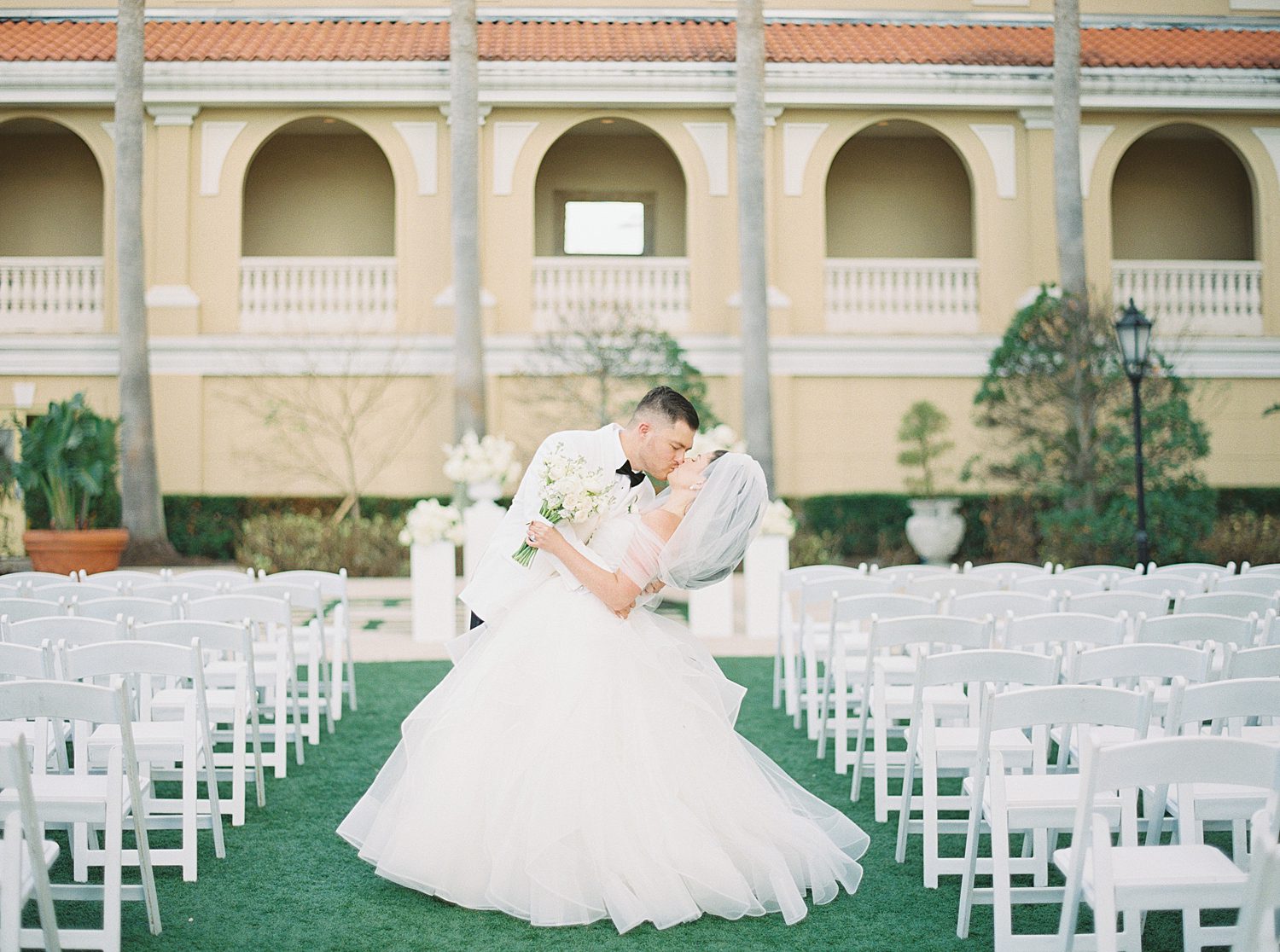 bride and groom kiss on lawn between white chairs at the Ritz Carlton Sarasota