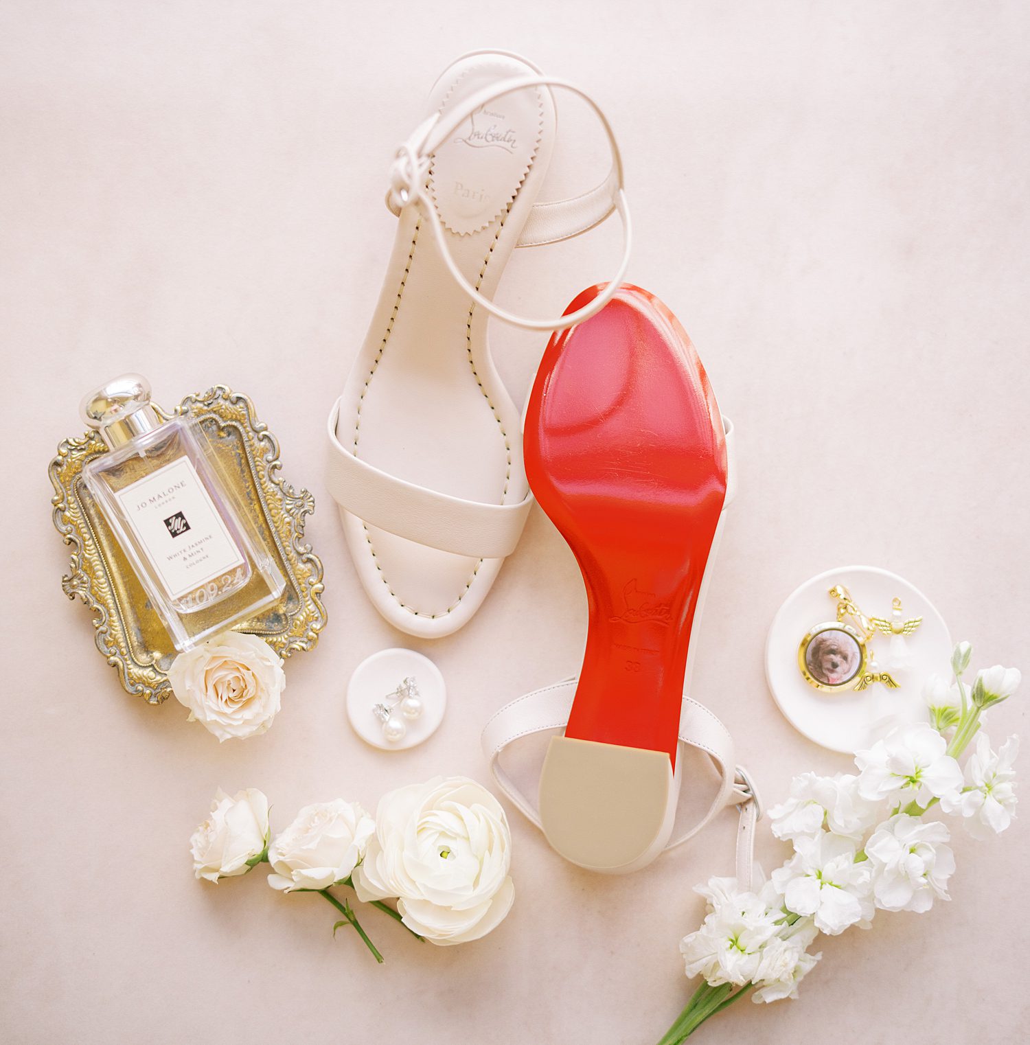 bride's shoes with red soles surrounded by white flowers on pink backdrop