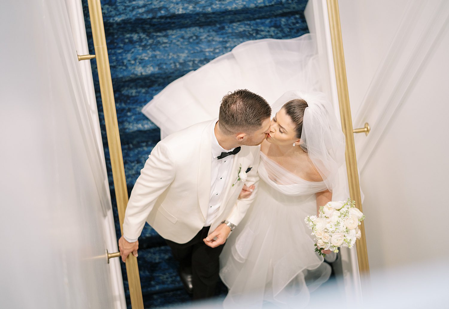 newlyweds kiss on blue velvet staircase during wedding day at the Ritz Carlton Sarasota